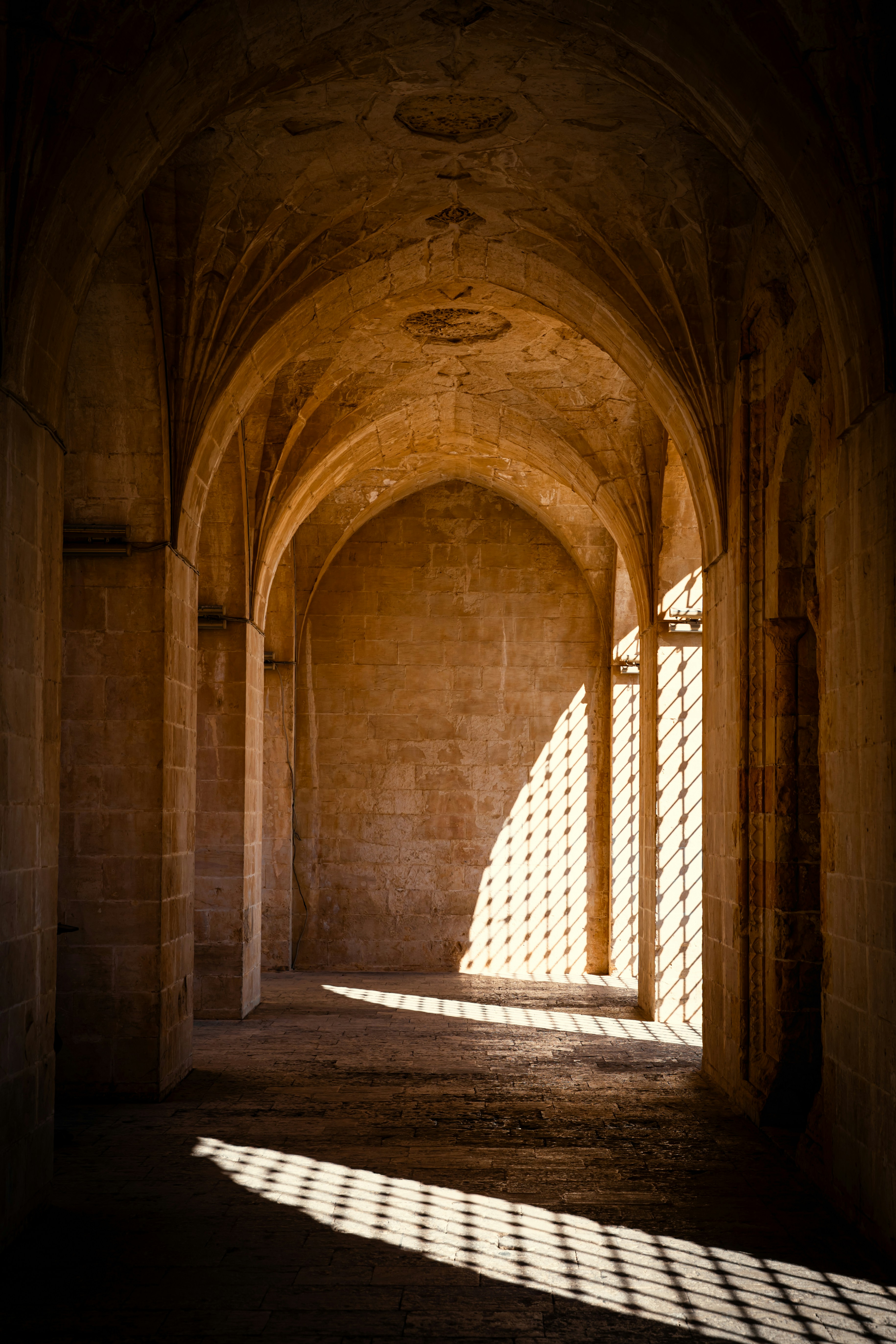 Sunlight streams through a patterned window into an arched hall.