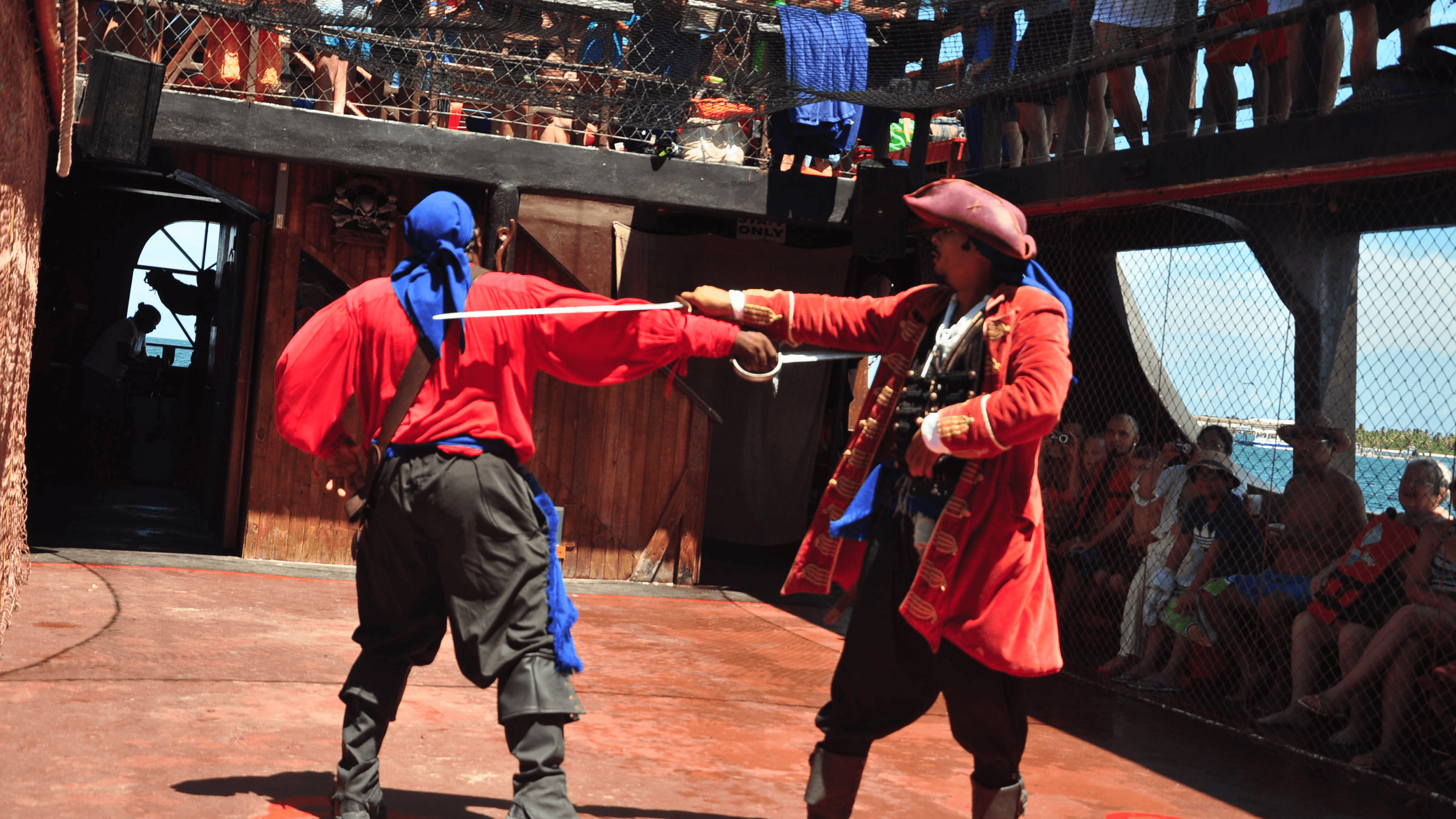 Two costumed pirates sword fighting on a ship deck in front of an audience