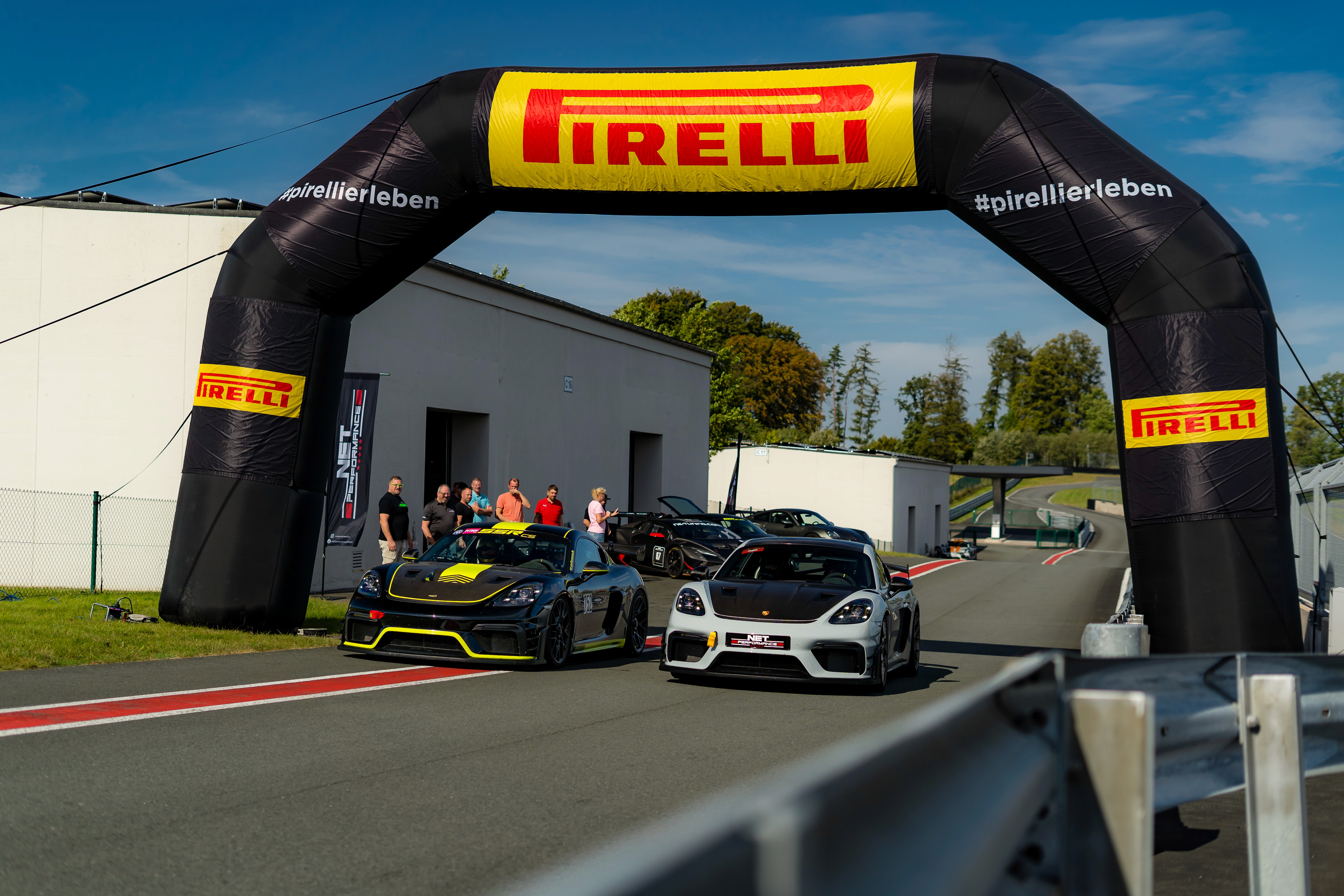 Zwei Porsche Sportwagen von NET Performance unter dem Pirelli-Torbogen der Rennstrecke