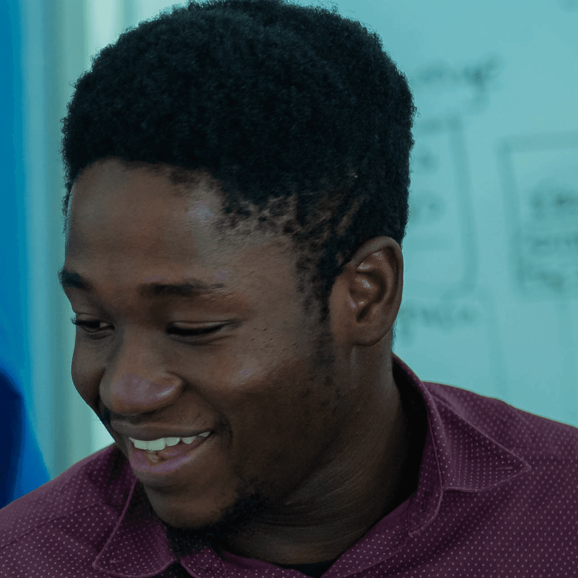Laughing young man in a maroon shirt with a light blue background.