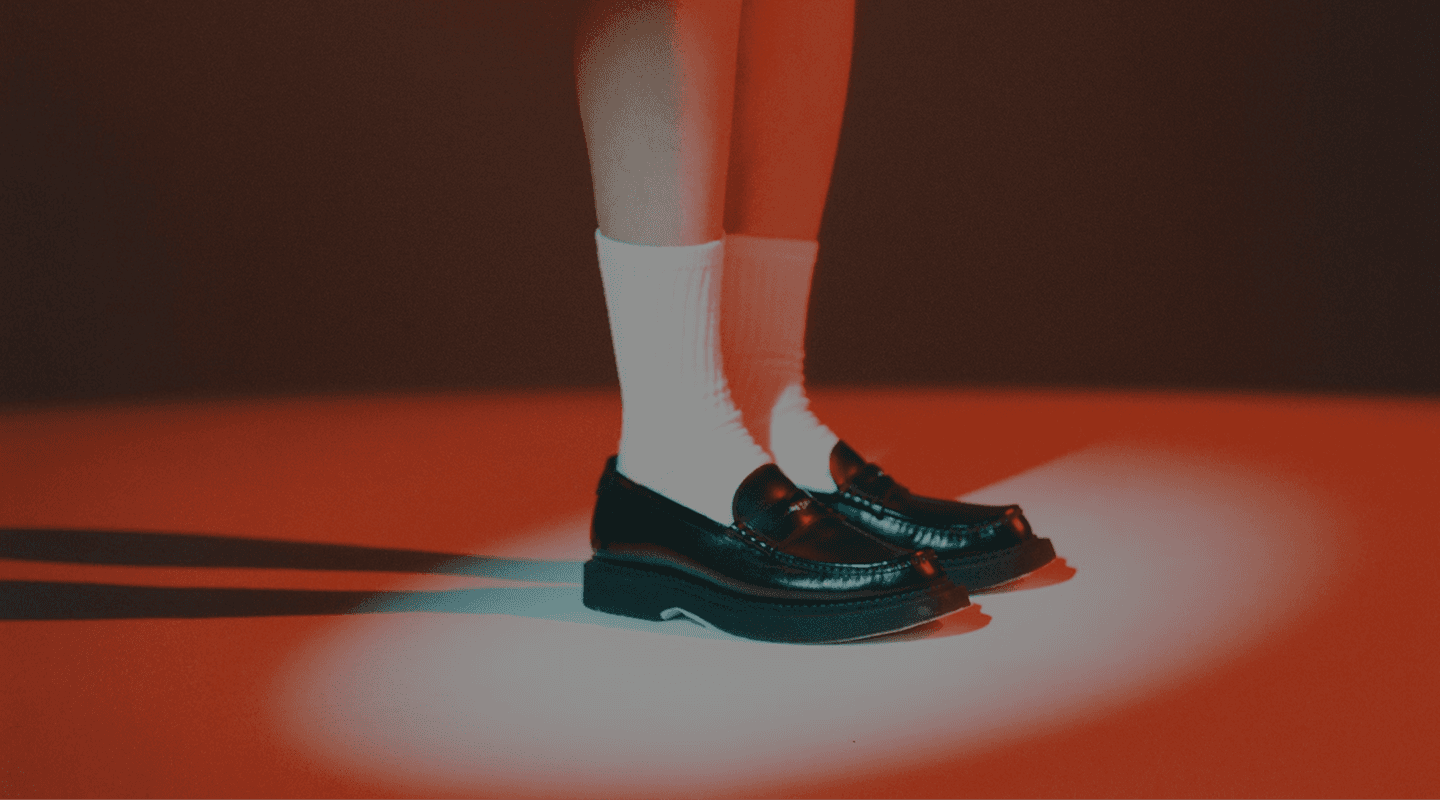 Close-up of black leather loafers worn with white socks, lit by red and blue lighting.