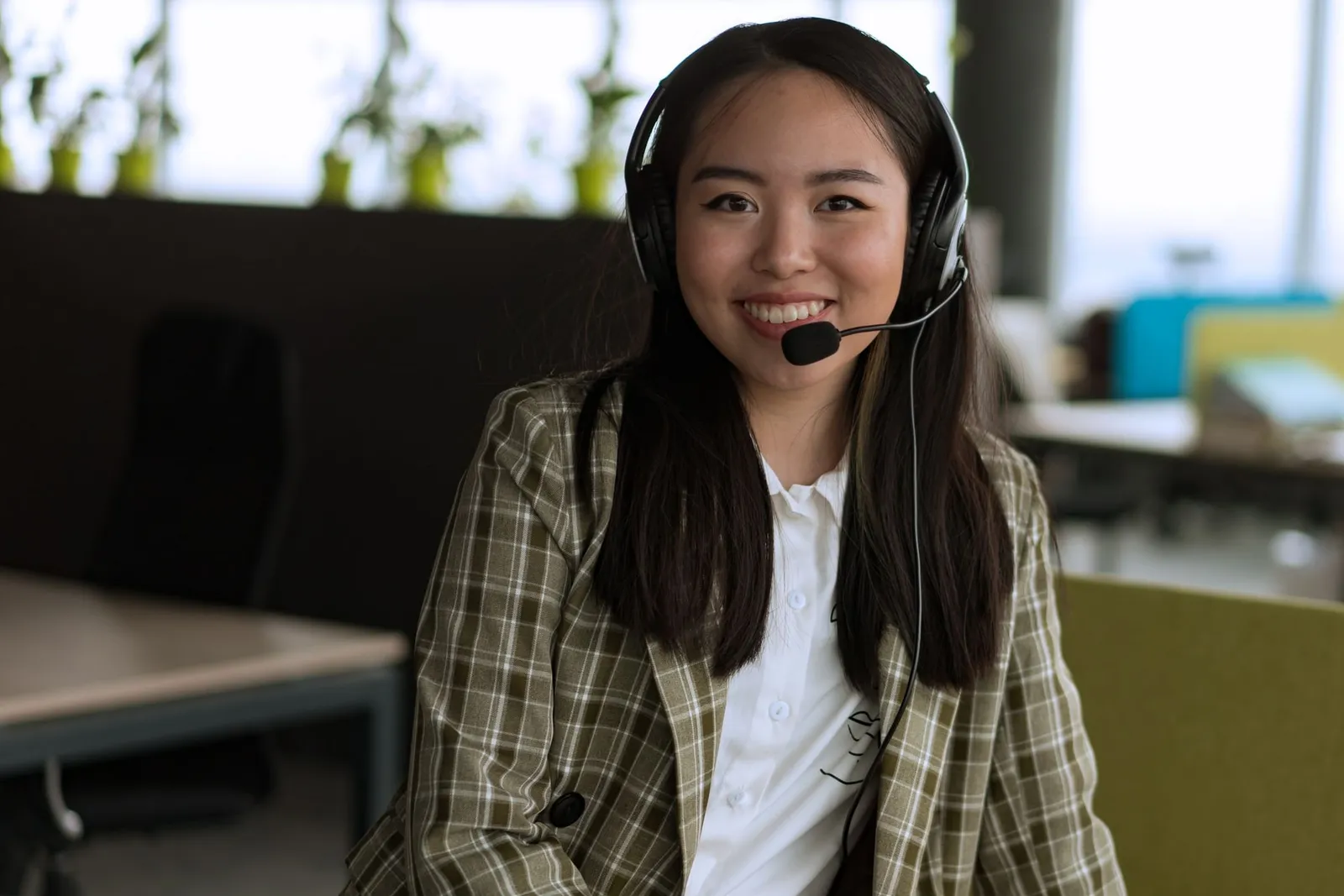 A support agent wearing a headset, smiling at her desk
