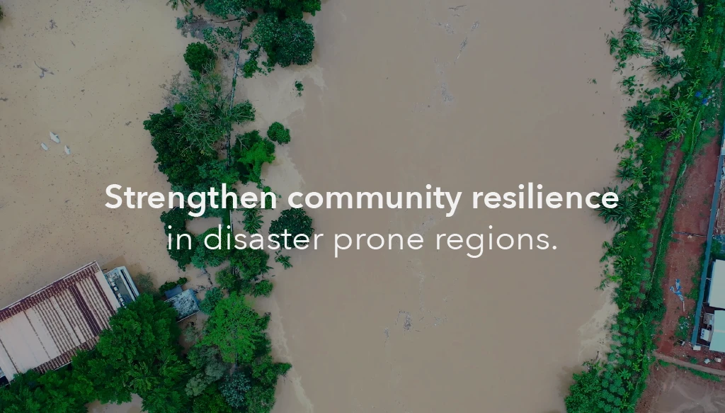 An image from a birds-eye view of a flood ravaging a town, with the text 'strengthen community resilience in diaster prone regions' inlayed