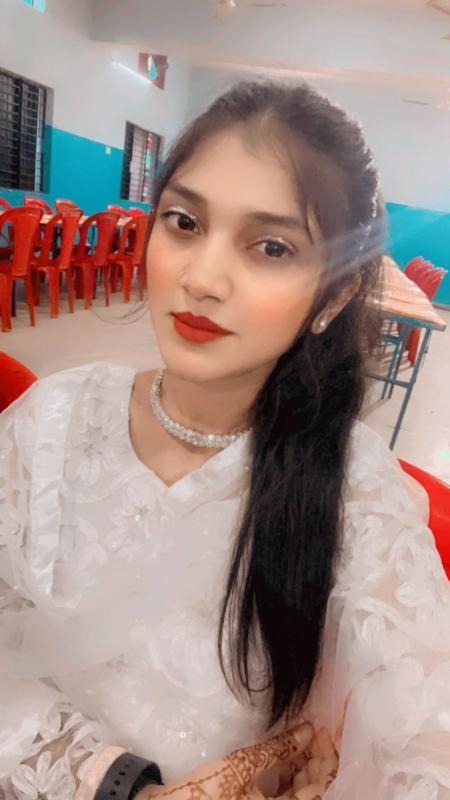 A smiling woman with her arms crossed, standing against a dark green background. She has long, dark hair.