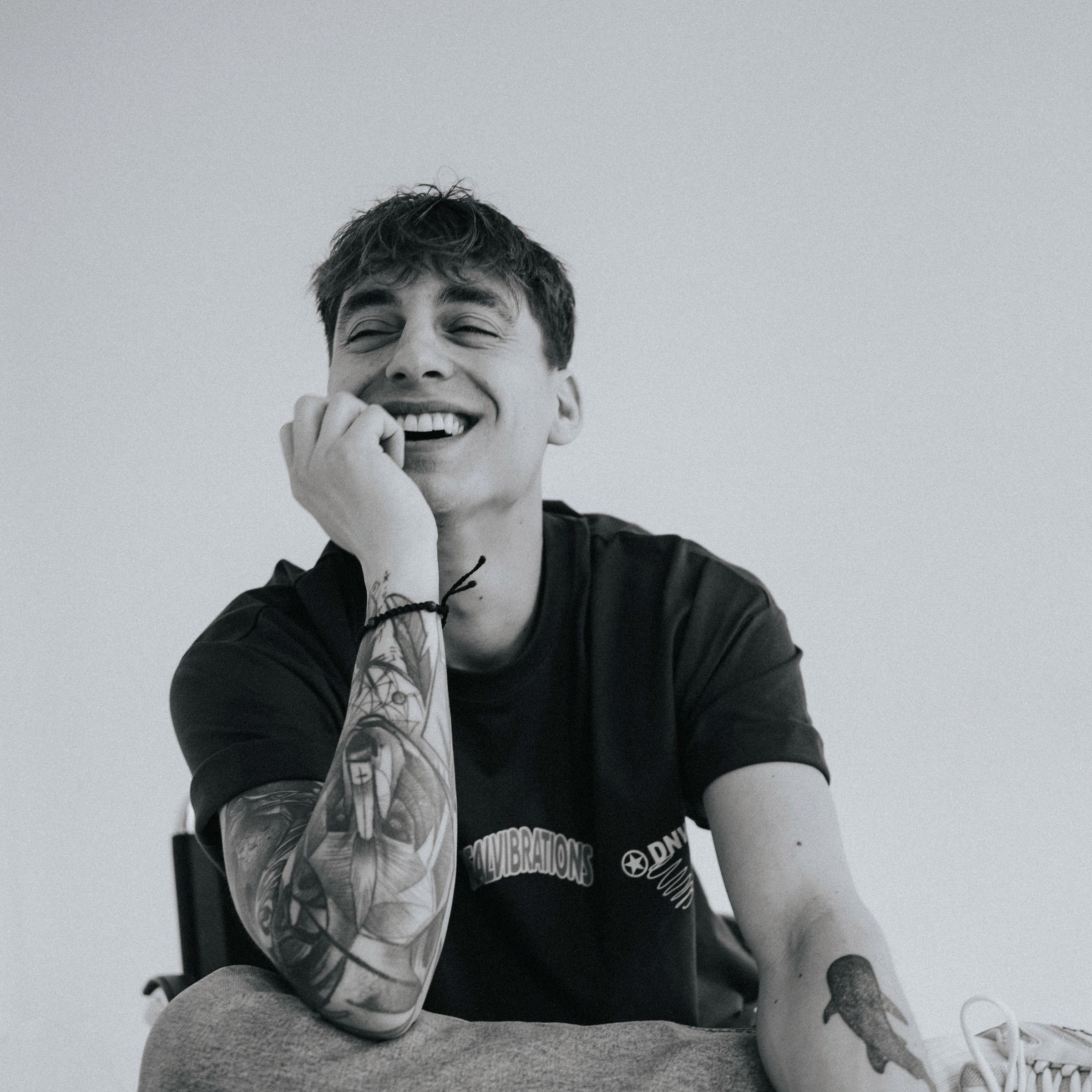 A thoughtful young person with dark hair gazes to the side, captured in soft black and white lighting.