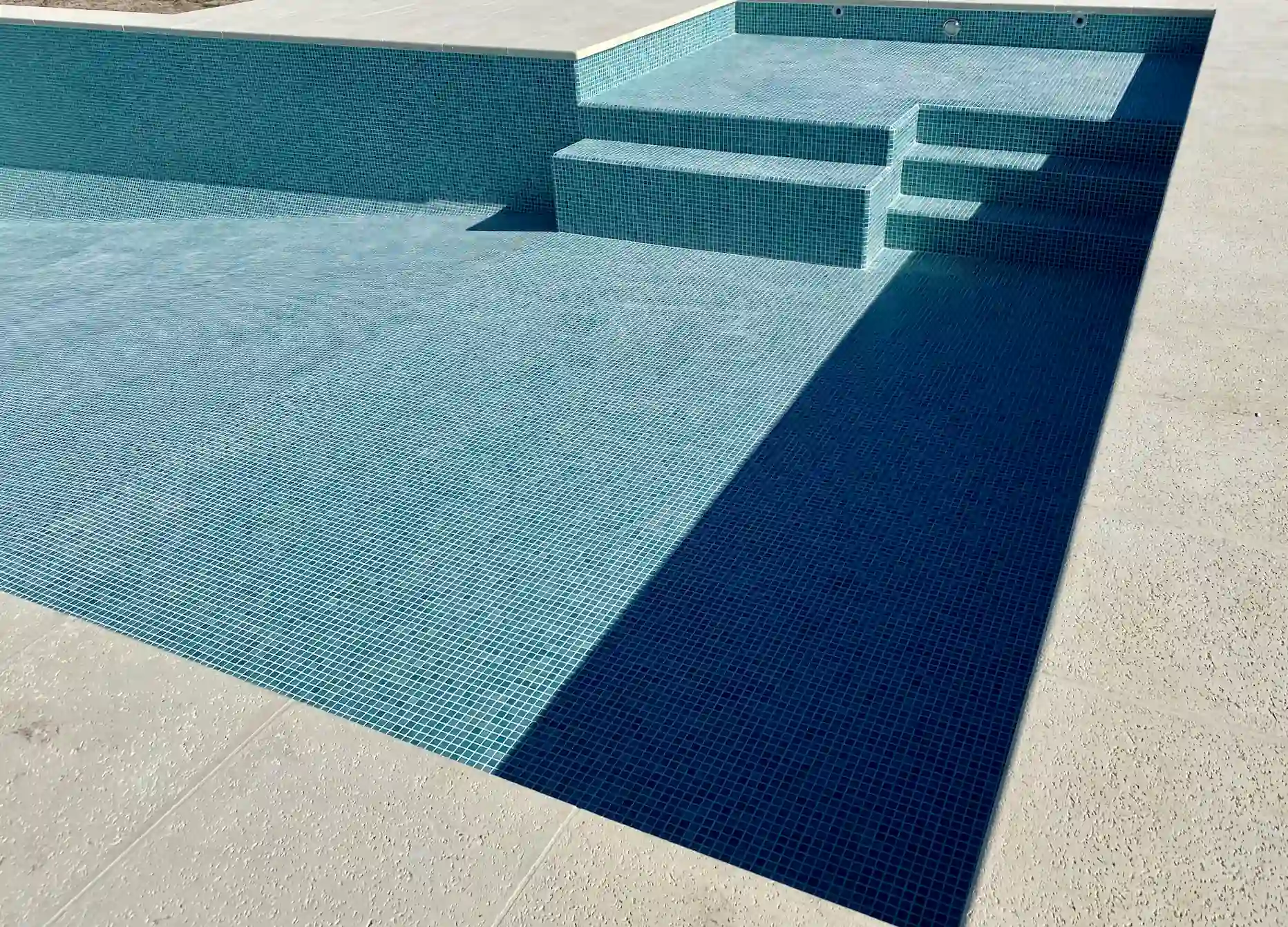 Escaleras de acceso a pileta de lujo revestida con venecitas importadas color turquesa, contrastando con un borde atérmico claro.