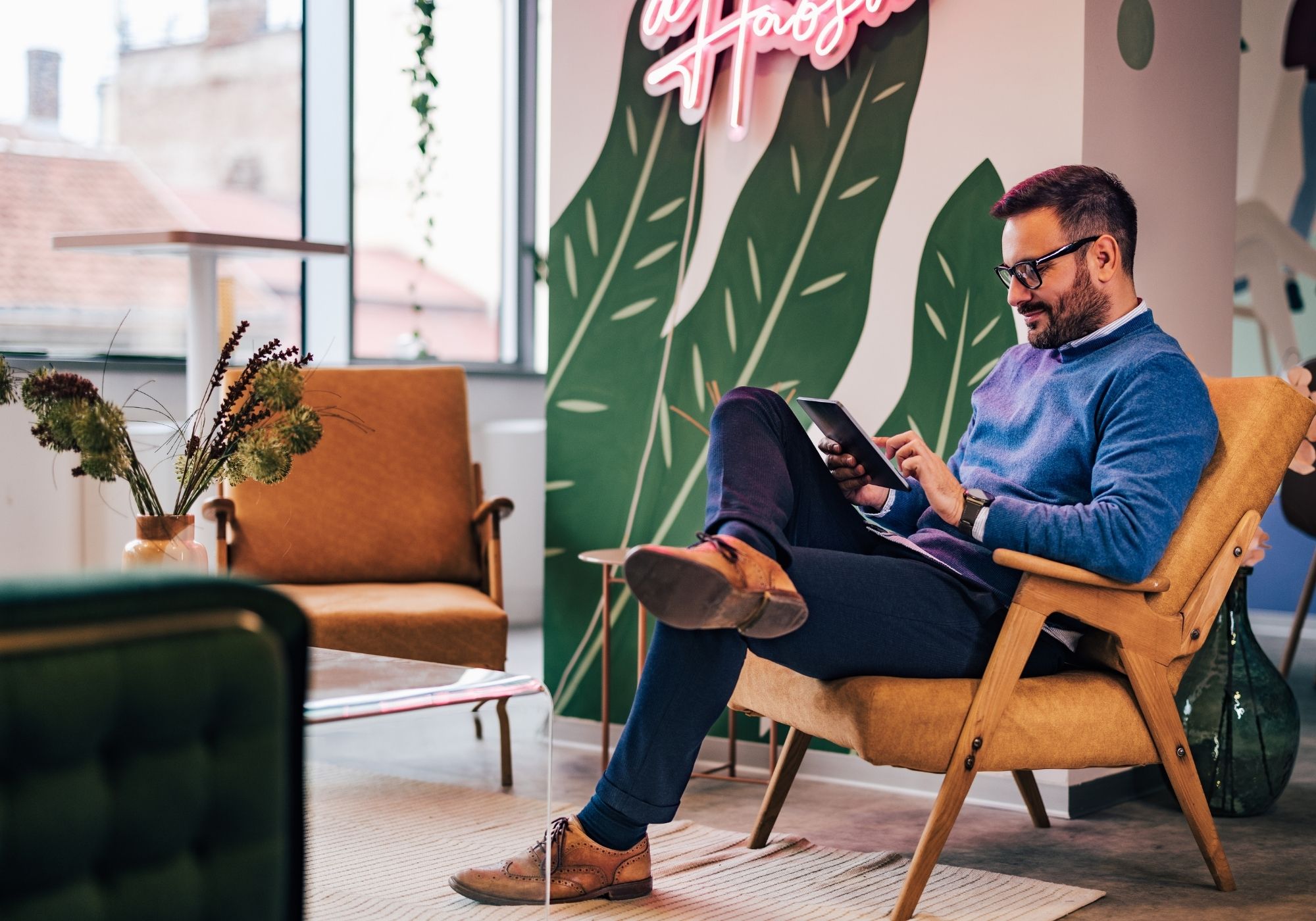 Man wearing headphones and a white t-shirt working on a laptop in soft natural light, with window shadows cast on the wall.