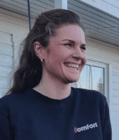 Blid dame i blå genser med Comfort logo foran hus