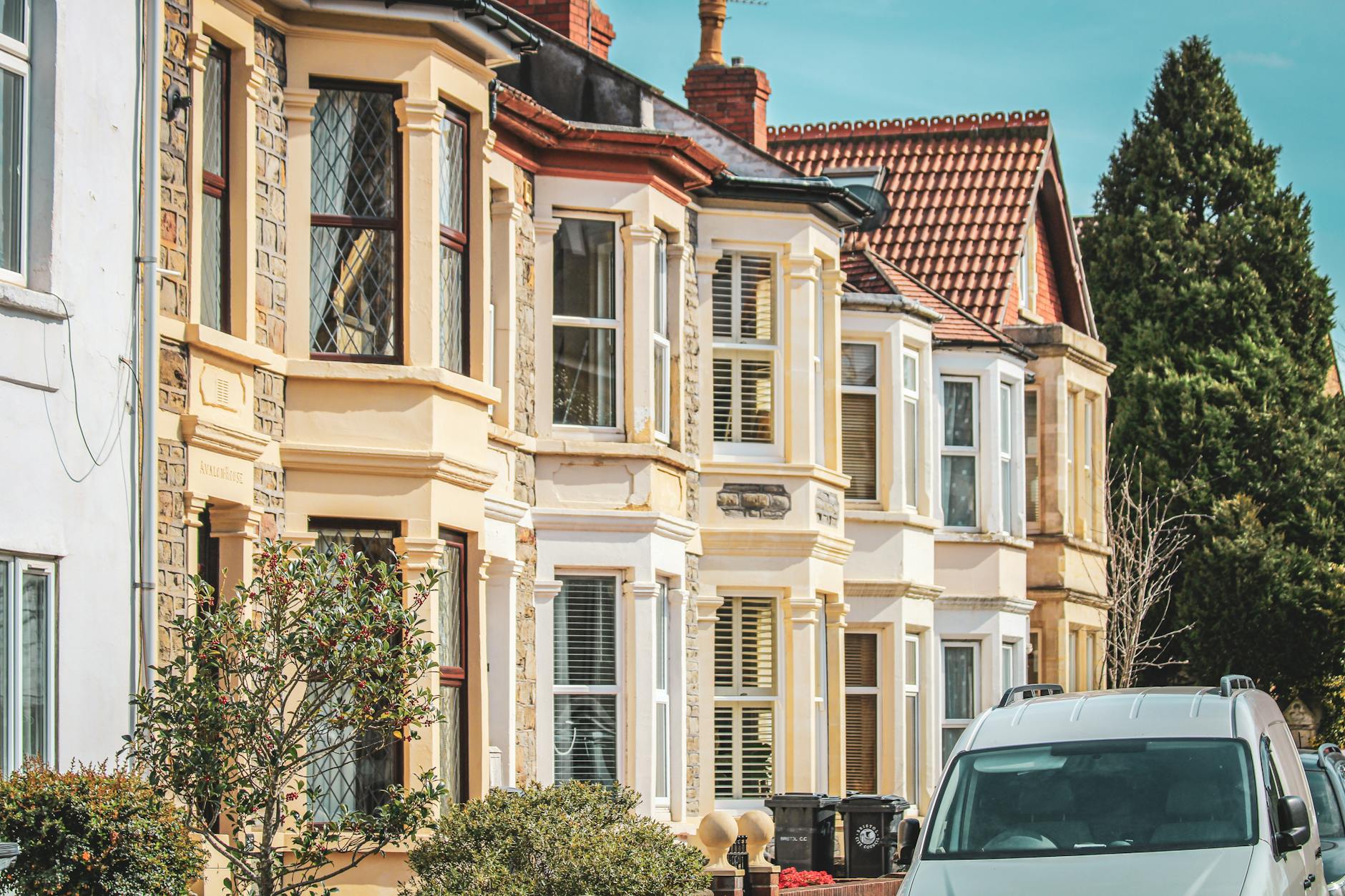 Row of Edwardian terraced houses with cream and stone facades and bay windows, white van parked outside under blue sky