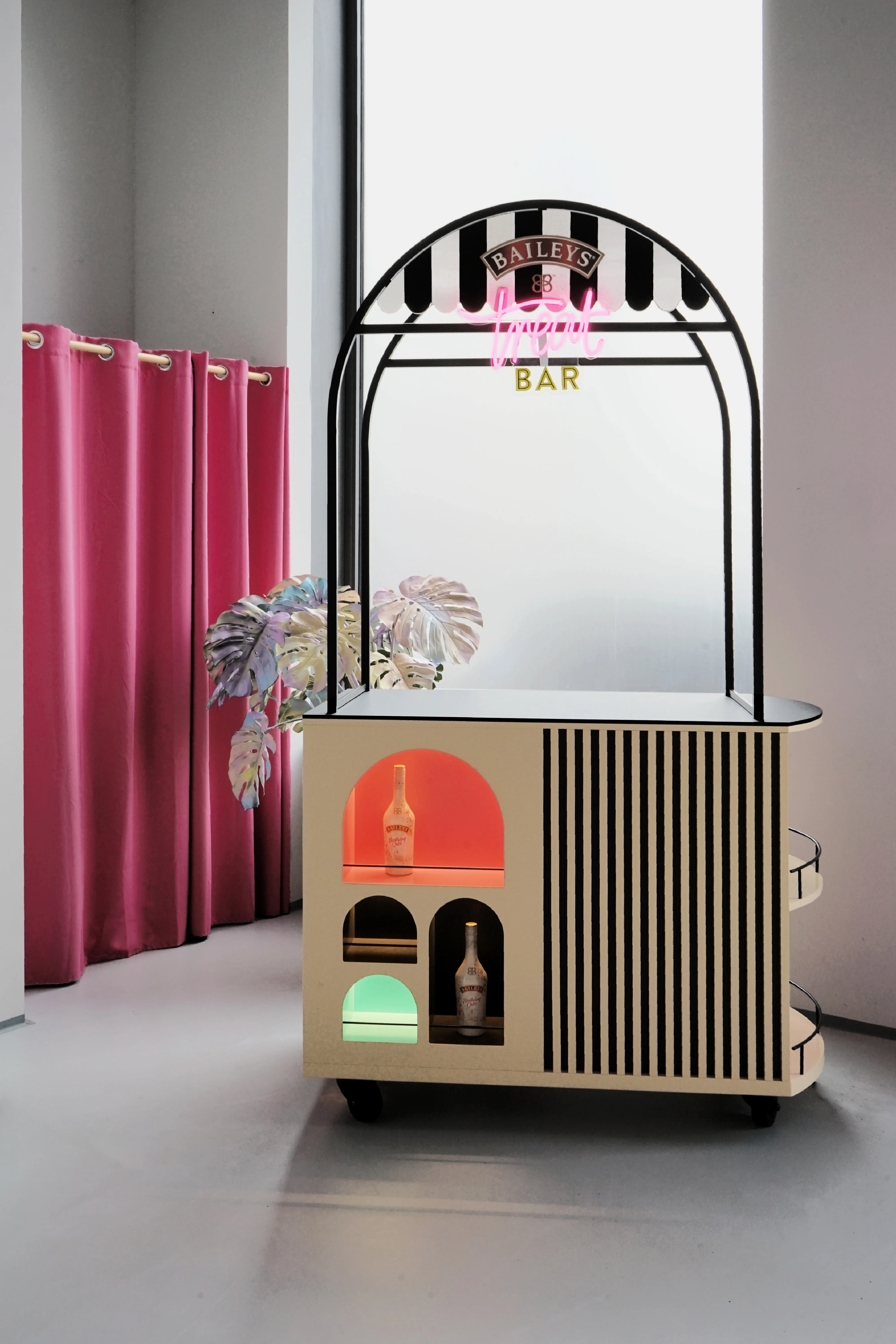 Mobile BAILEYS Treatbar with striped awning arch, pink neon lettering, cream body with arched niches in red and green and a pink curtain beside it.