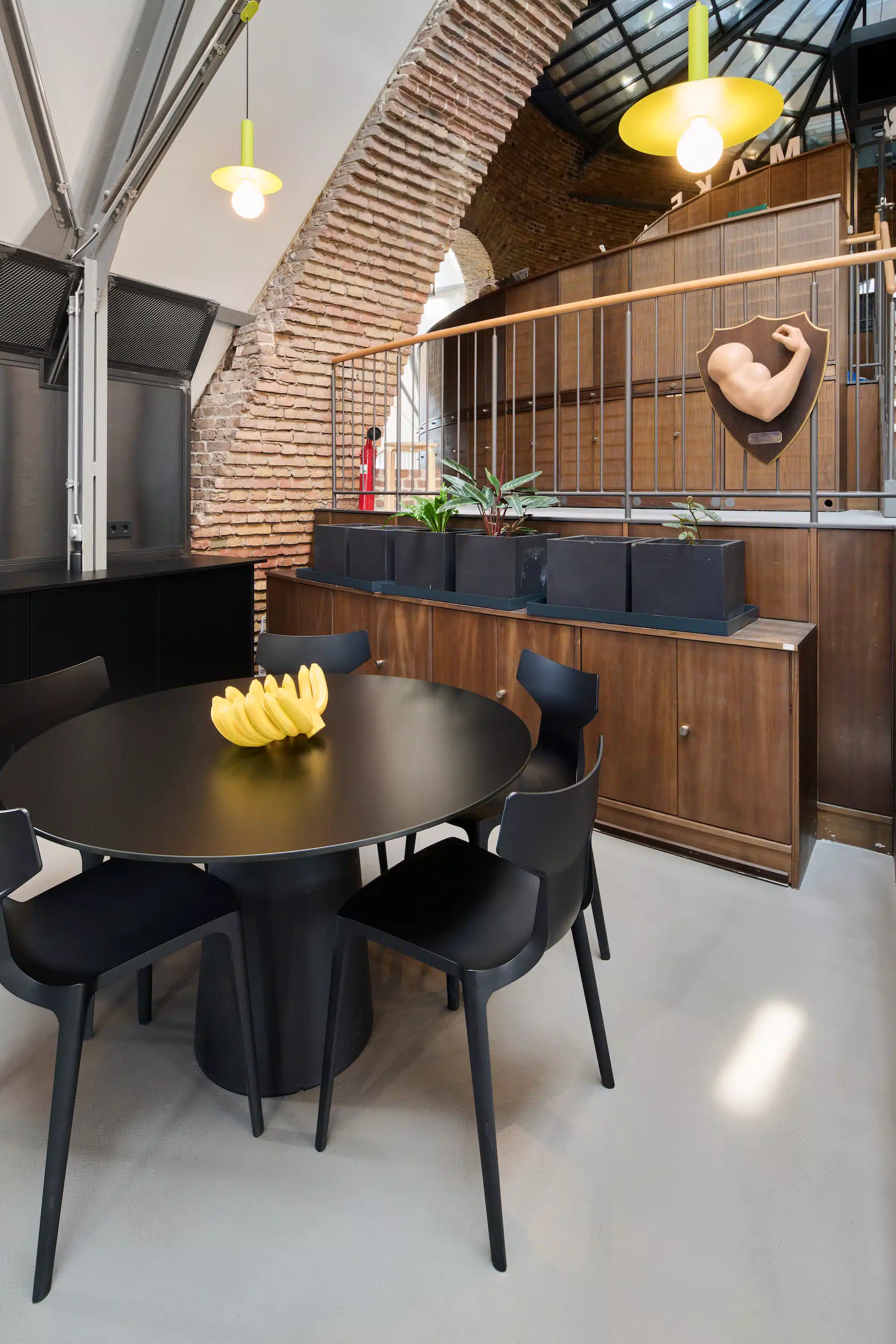 Dojo Office – dining area with round black table under brick arch, yellow pendant lamps and decorated wall shelves