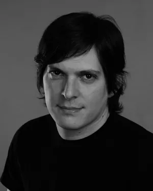 Smiling blonde woman with freckles in a white shirt, arms crossed, minimalist studio portrait.