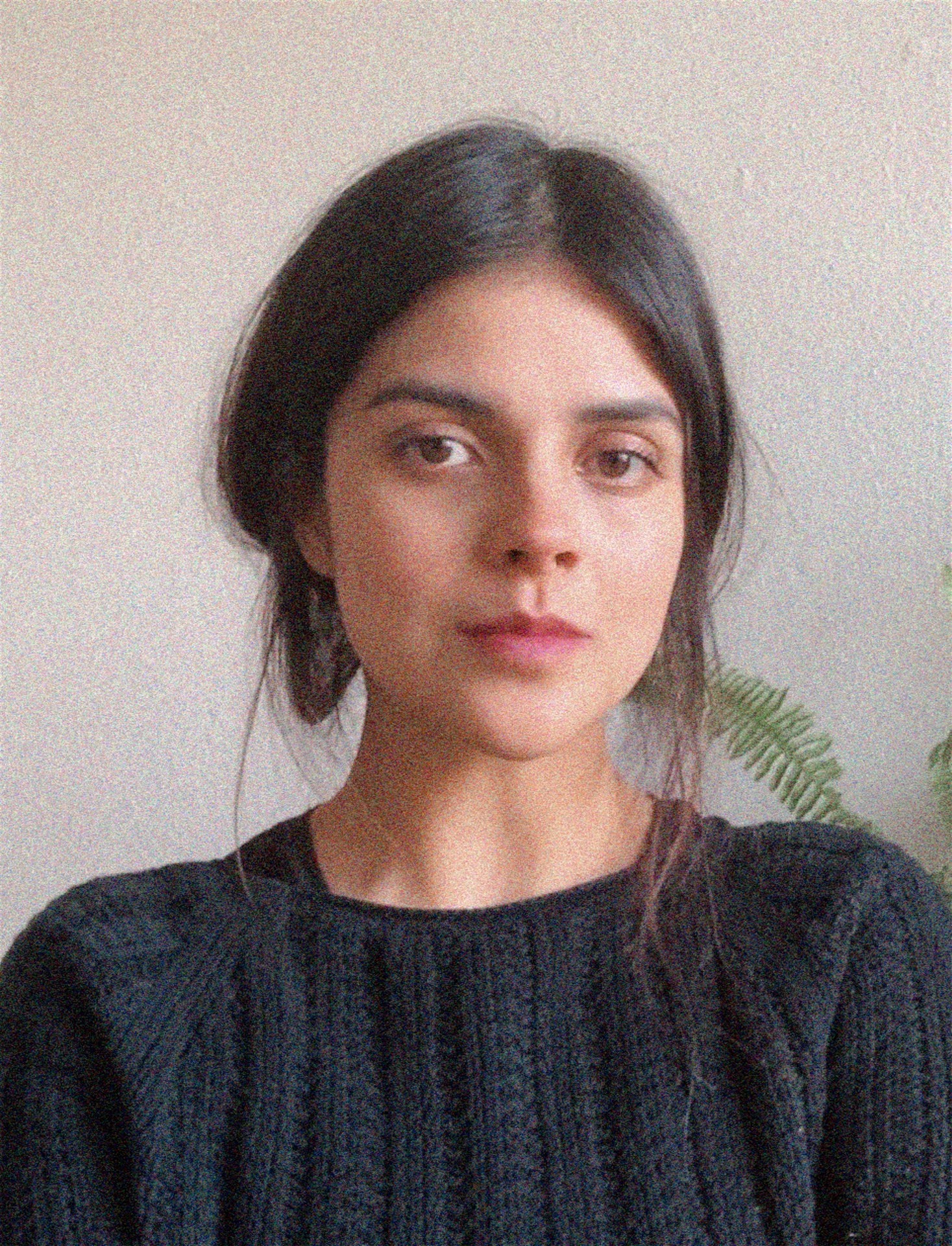 Person wearing a blue puffer jacket and red backpack standing in front of a light blue building on a city street.