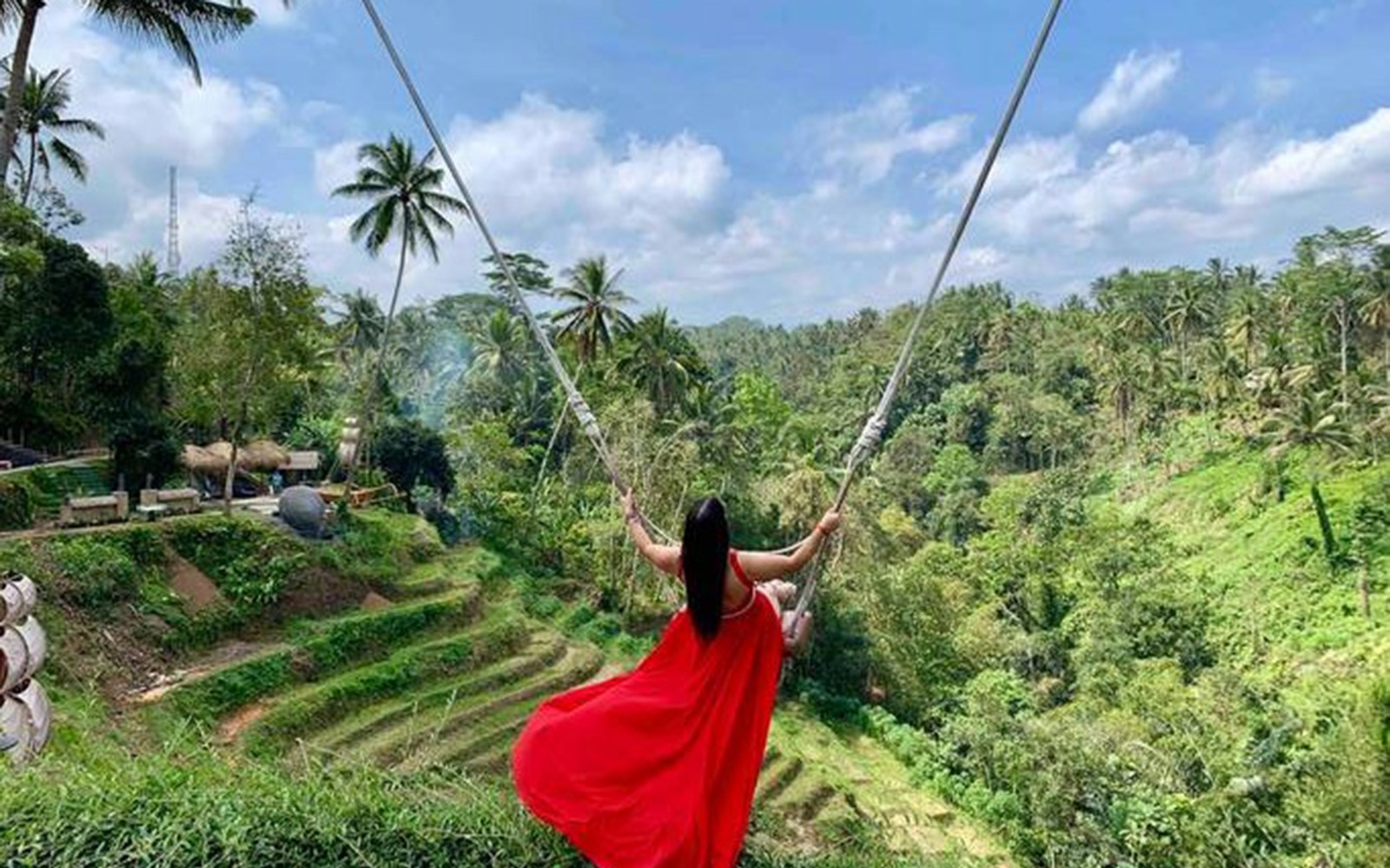 Person on swing overlooking Bali rice terraces and jungle.