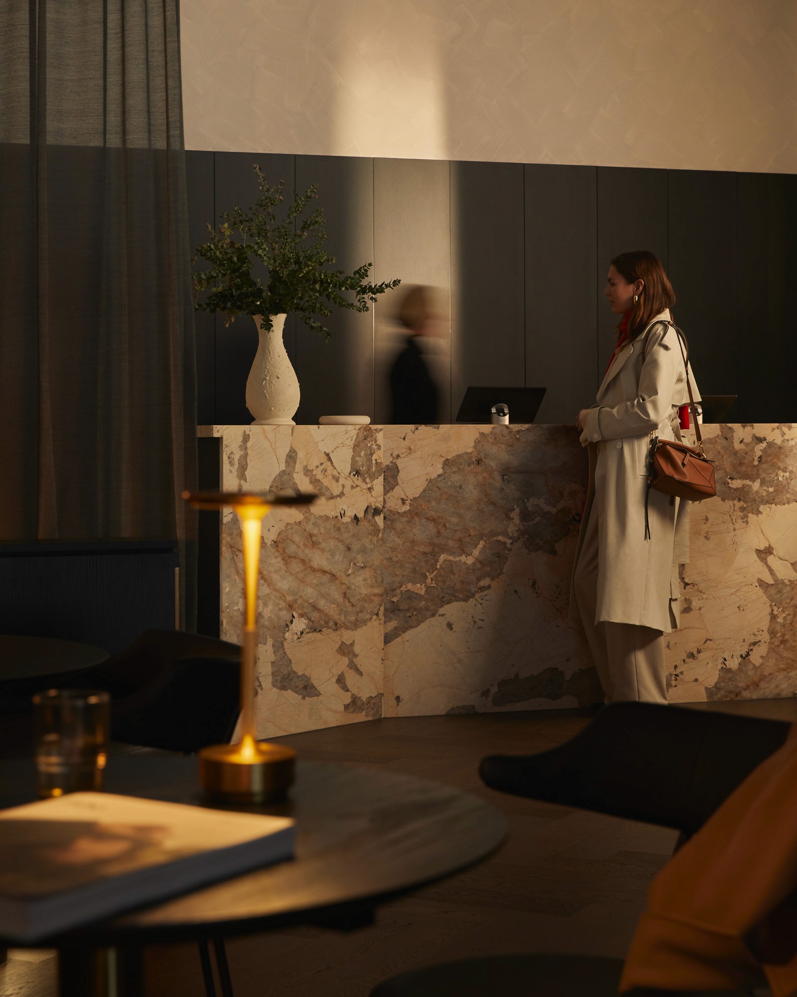 Awoman in an elegant coat approaching a reception desk at Eclat's members lounge.