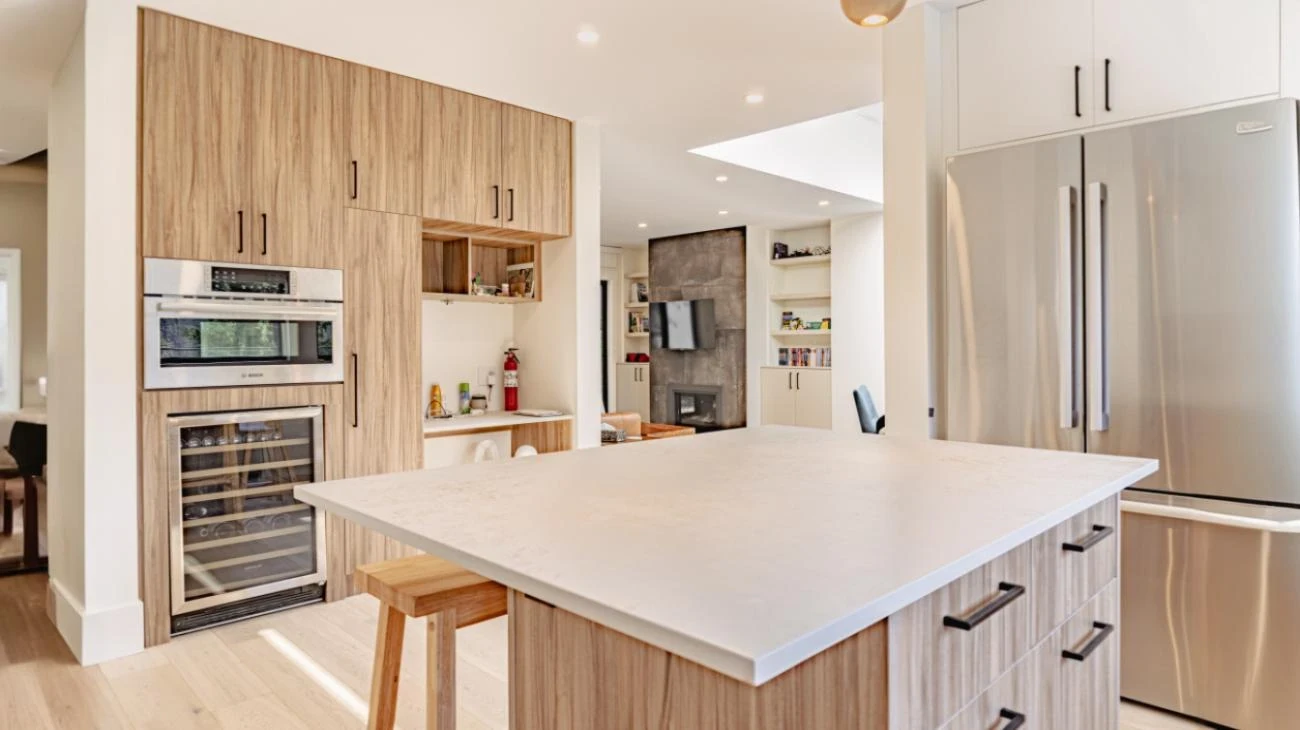 Luxury custom kitchen design with wood-grain cabinetry, white quartz countertops, wine fridge, and view to living room fireplace in Vancouver
