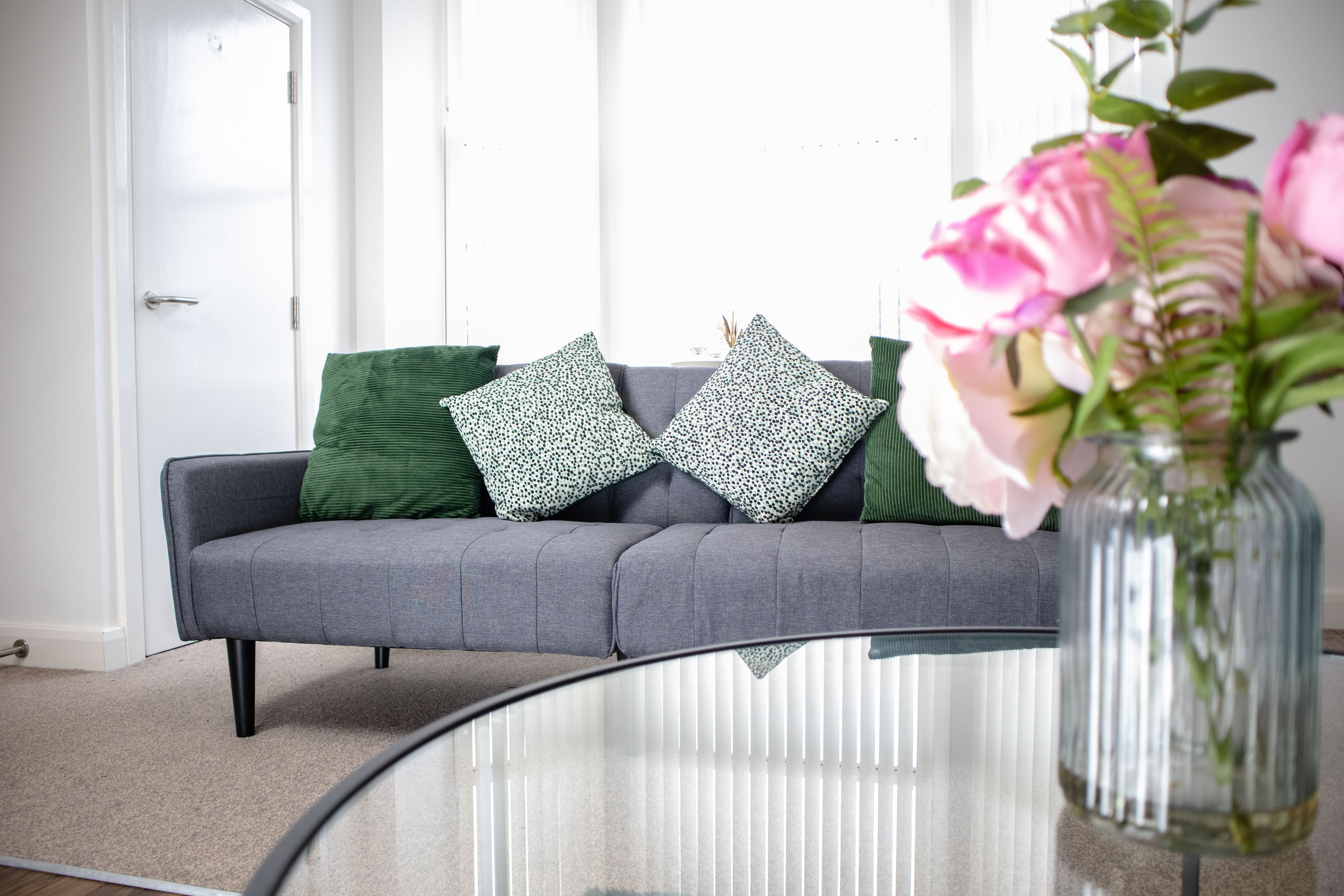 Bright simple Airbnb photography with a grey couch and flowers in a vase on a glass table