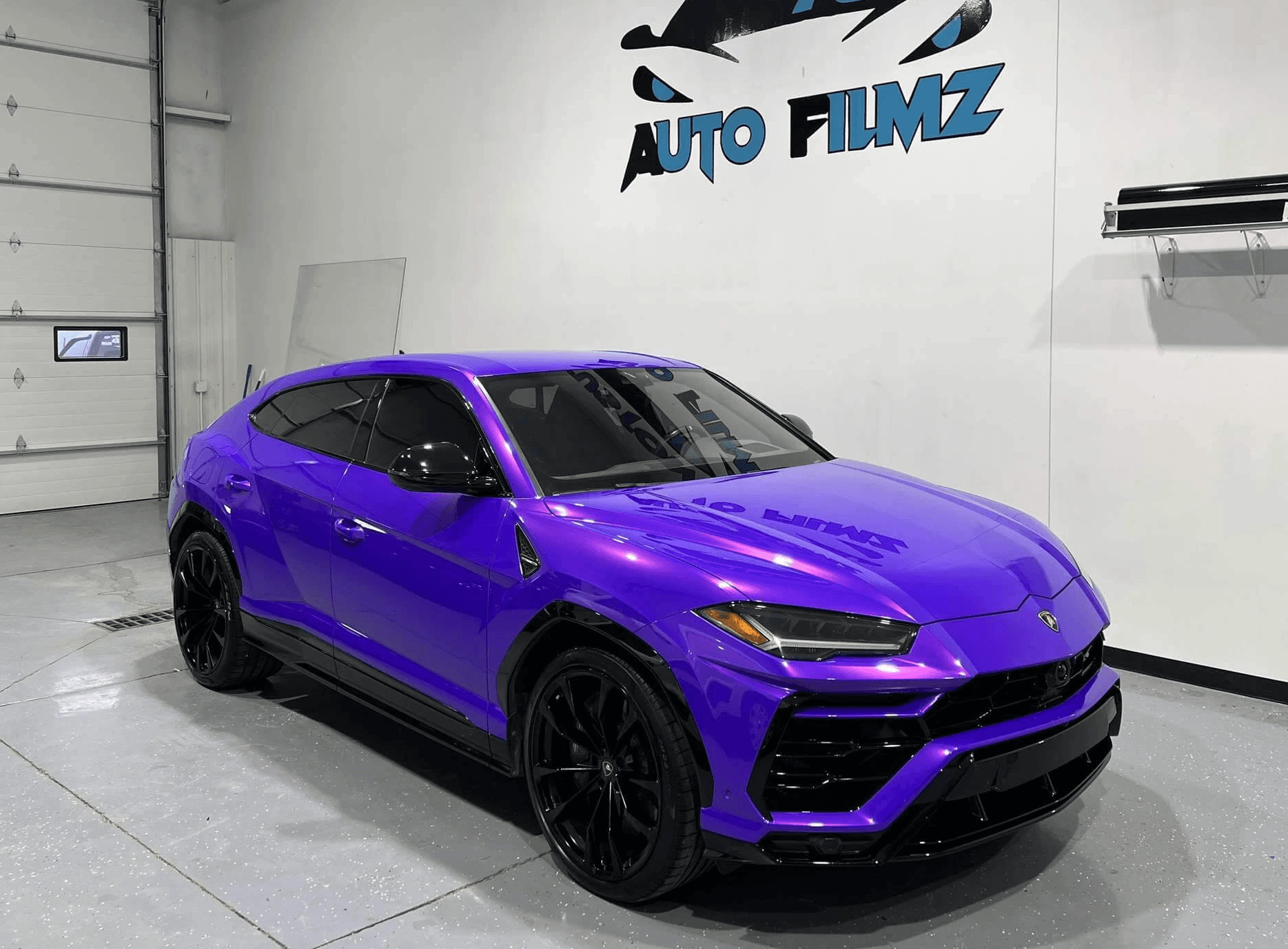 A vibrant purple Lamborghini Urus is parked indoors on a polished concrete floor.