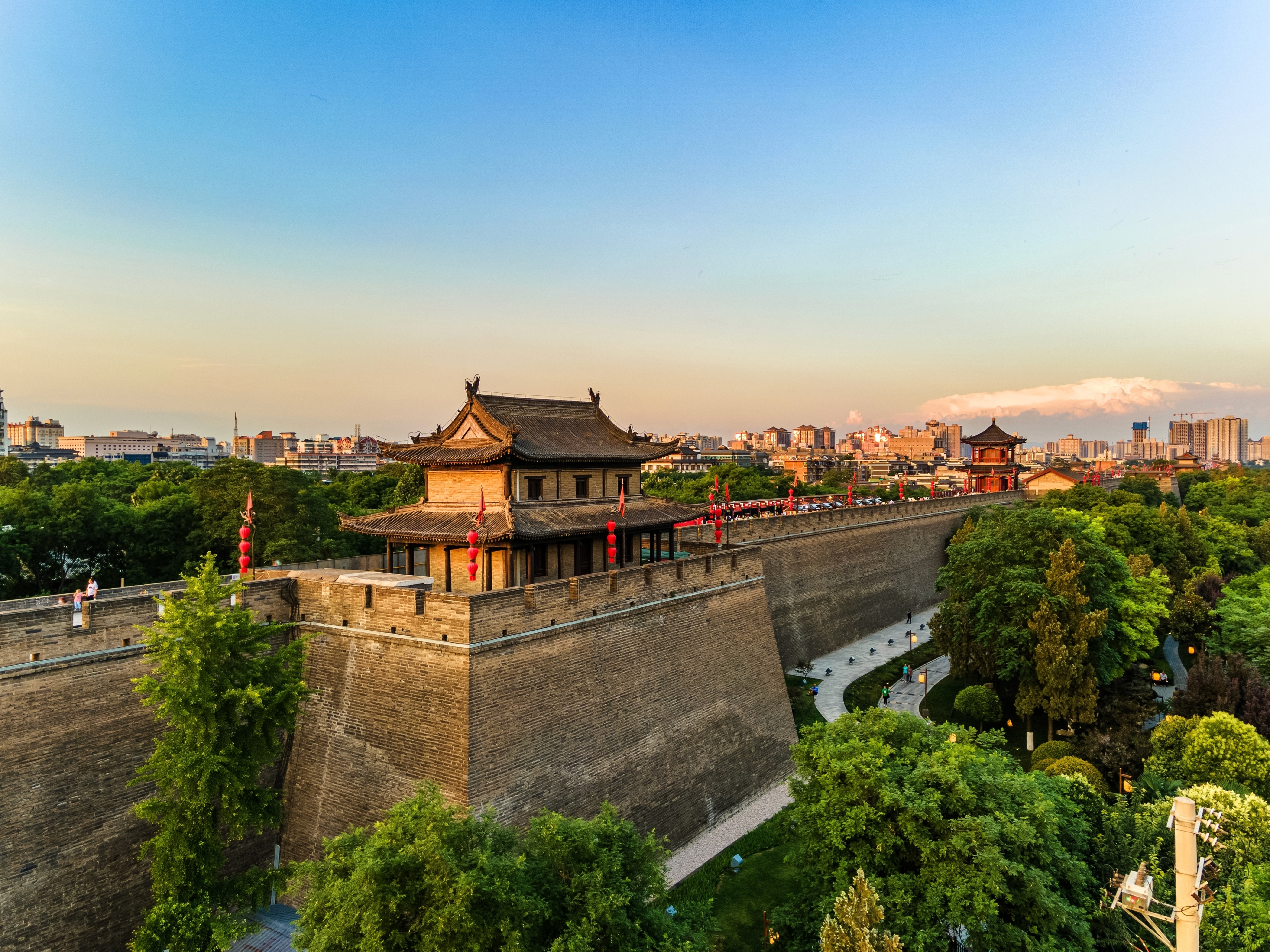 The high, sheer, fortified wall of Xi'an City, with high-rise buildings in the distance and green trees on the outside of the wall