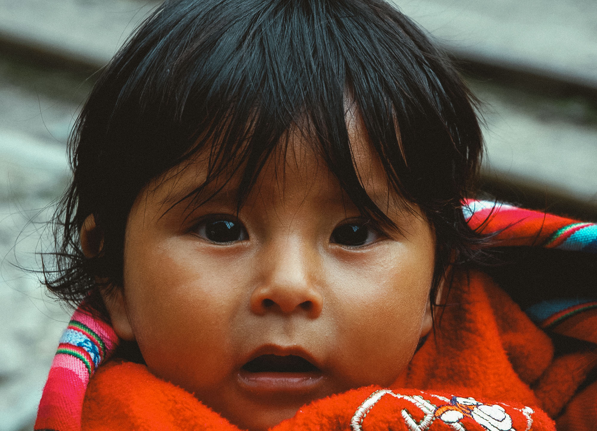 Kind in Cusco, Peru, der ein Alpaka hält. Die Aufnahme betont die starken Texturen der traditionellen Kleidung und die authentischen Gesichtszüge vor den historischen Steinmauern der Stadt.