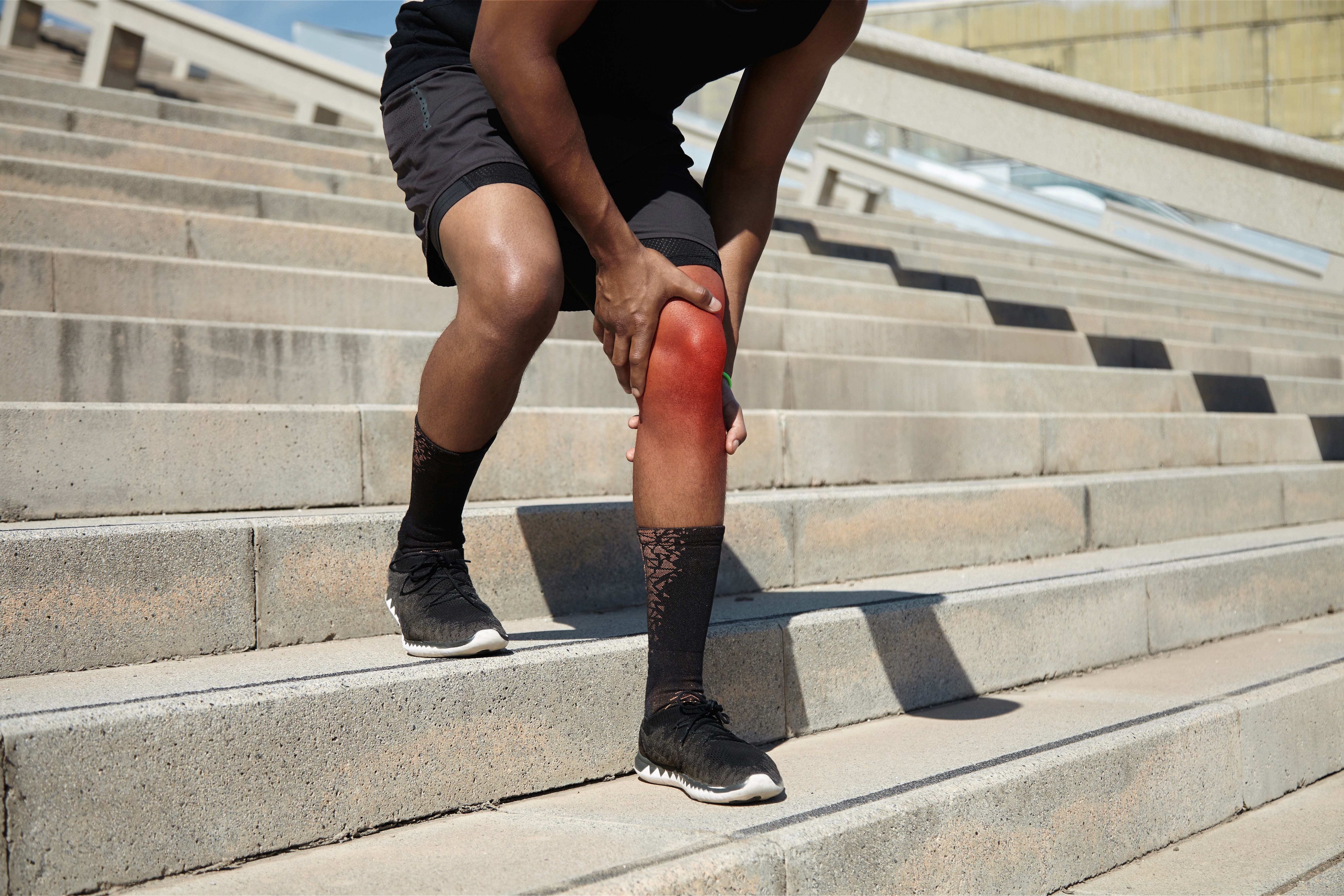 運動員於戶外樓梯因膝關節疼痛（Knee Pain / Runner's Knee）扶膝休息，紅光標示膝蓋髕骨與內側關節發炎及受傷痛點