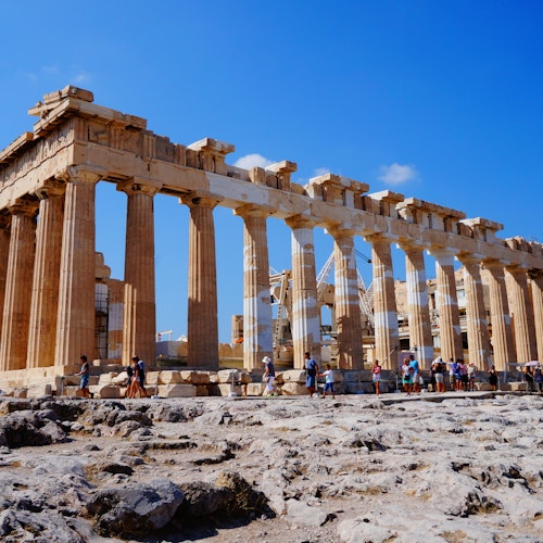 游客们在希腊雅典的帕特农神庙游览,在晴朗湛蓝的天空下,古老的石柱后方可见脚手架。