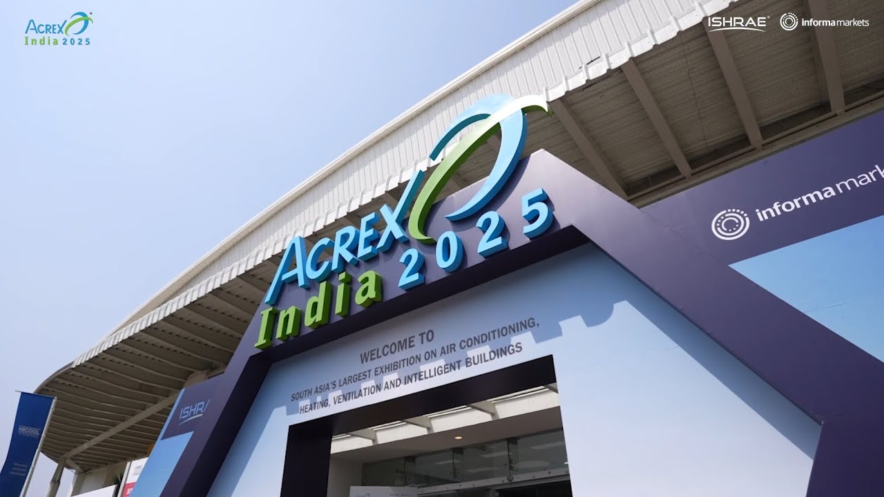 A man stands while two people sit at a table in an office setting, smiling and engaged in conversation. The mood is friendly and collaborative.