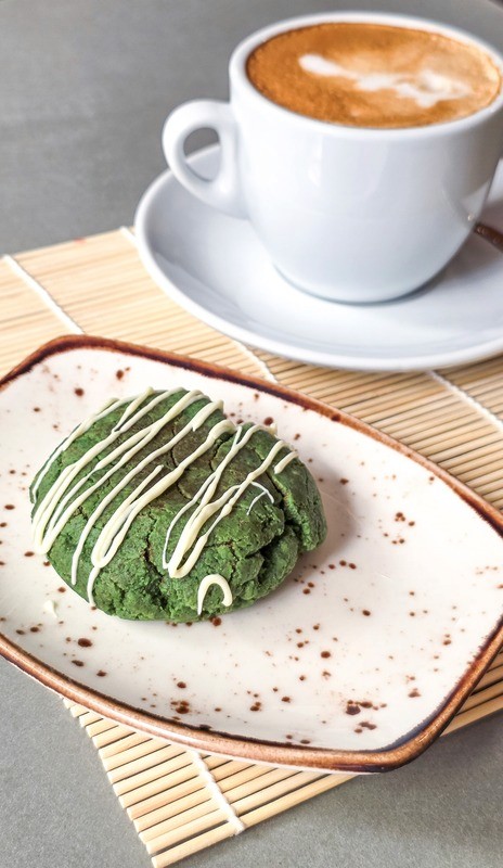 Matcha cookie drizzled with white icing, served alongside coffee