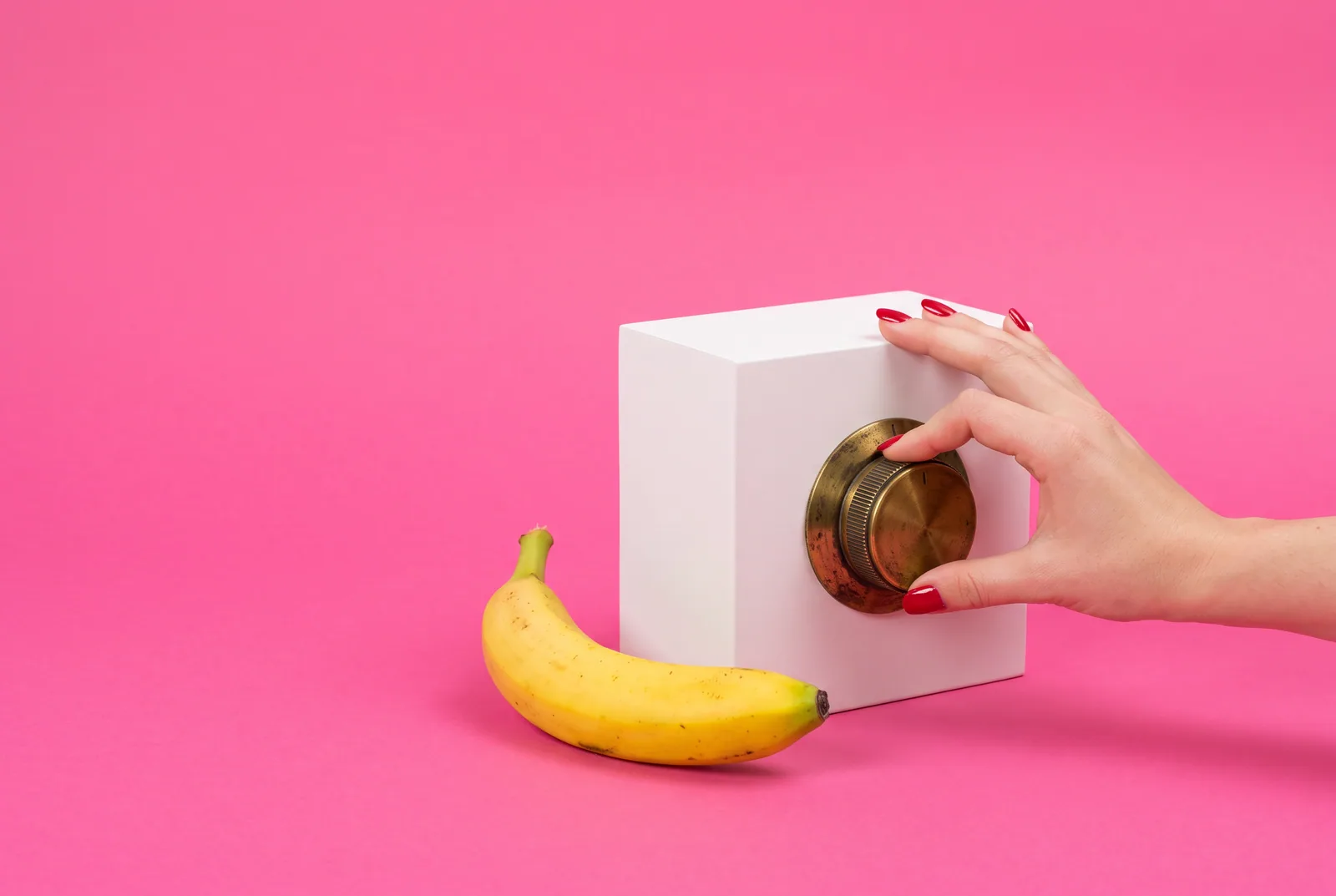 A hand with red nails turning a large brass dial next to a banana, changing the DNS setting to block porn on a router