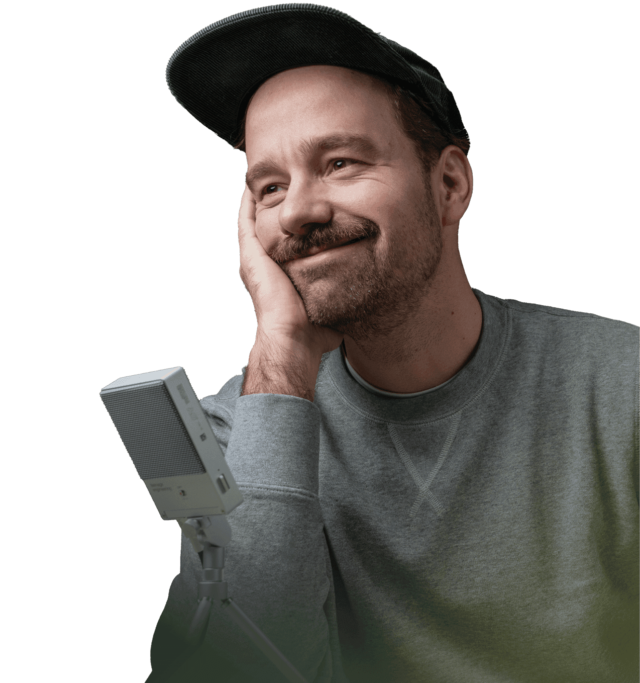 Prowadzący kurs Framera - Tomasz Biskup. Uśmiechnięty mężczyzna w czapce i szarej bluzie, opiera policzek na dłoni i patrzy w bok. Przed nim mikrofon studyjny.