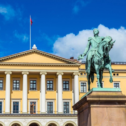 Statue of a man on a horse in front of a yellow building with columns. A flag is flying atop the building under a blue sky.