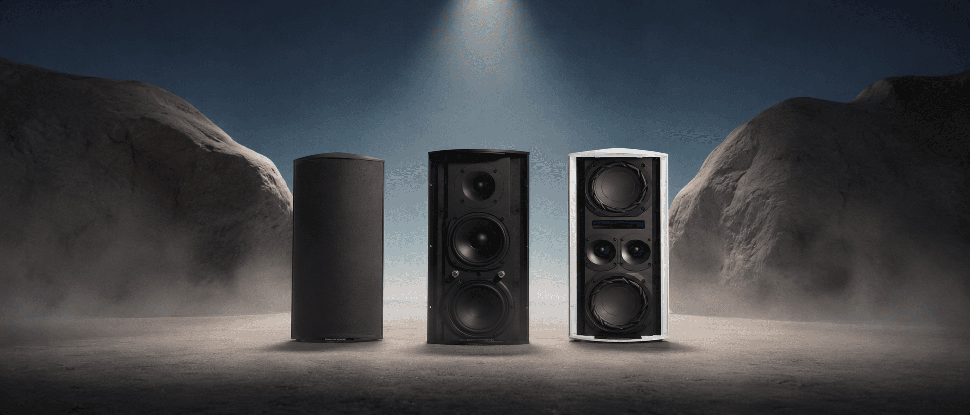 Three floor-standing speakers in a stark landscape.