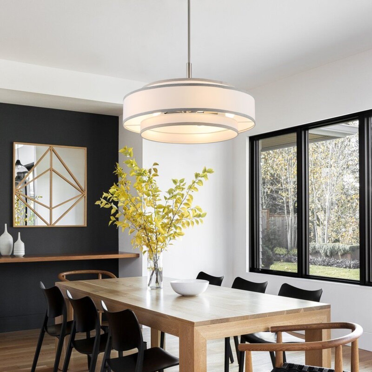 White drum chandelier over rectangle wood table with six black chairs.