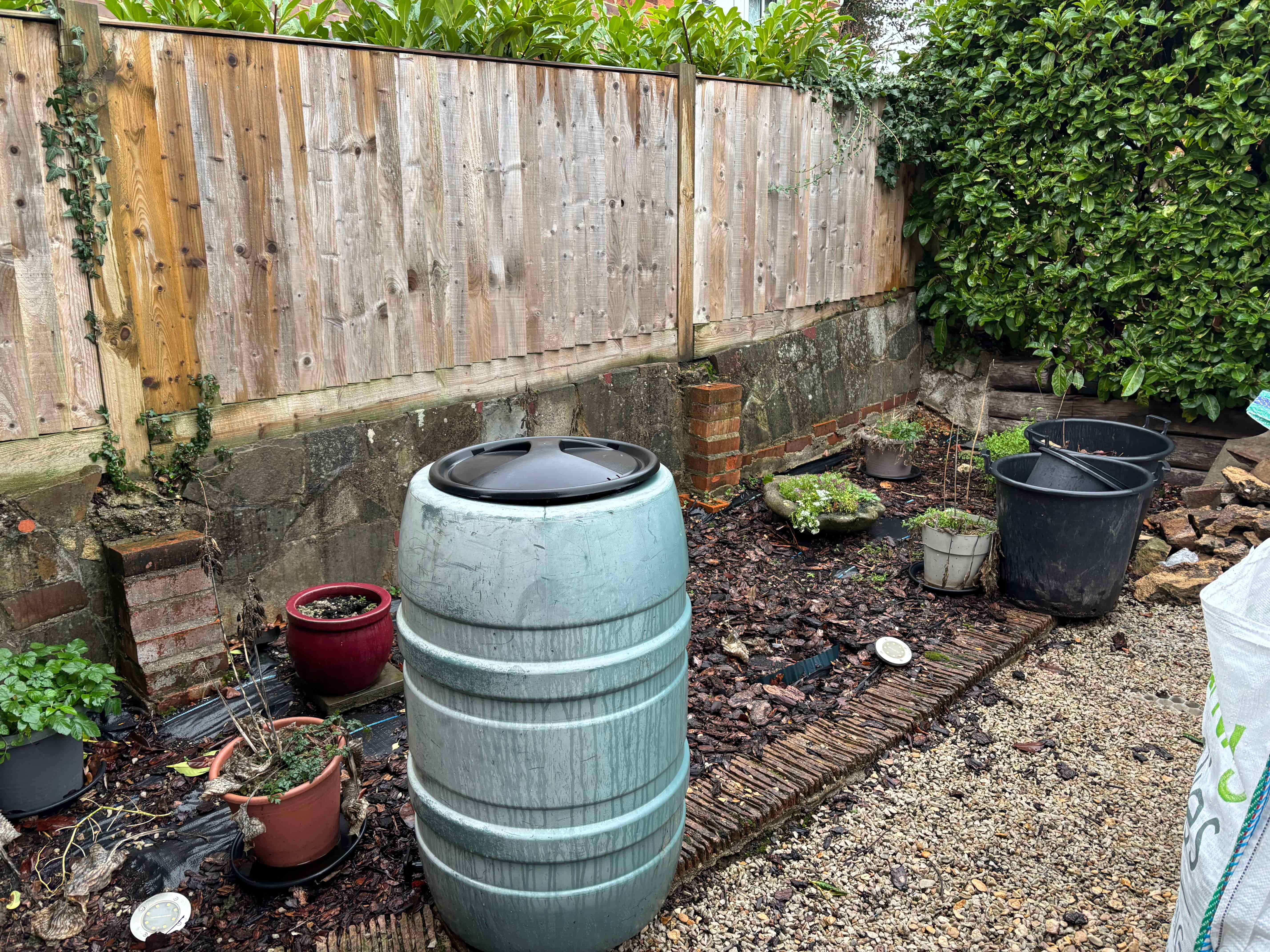 : Garden path through modern black wooden pergolas leading to a green shed.