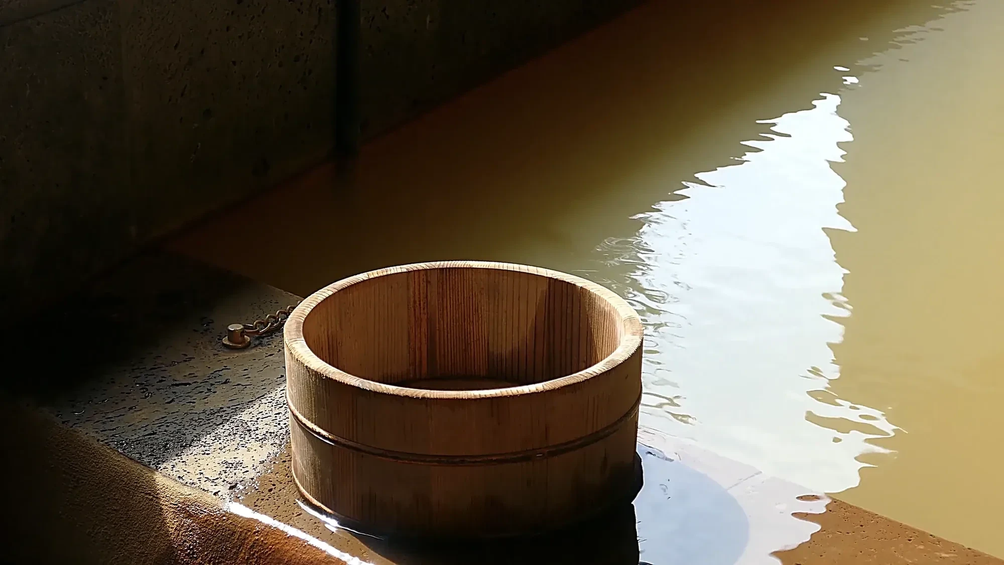 A wooden bucket at the edge of an amber hot-spring pool