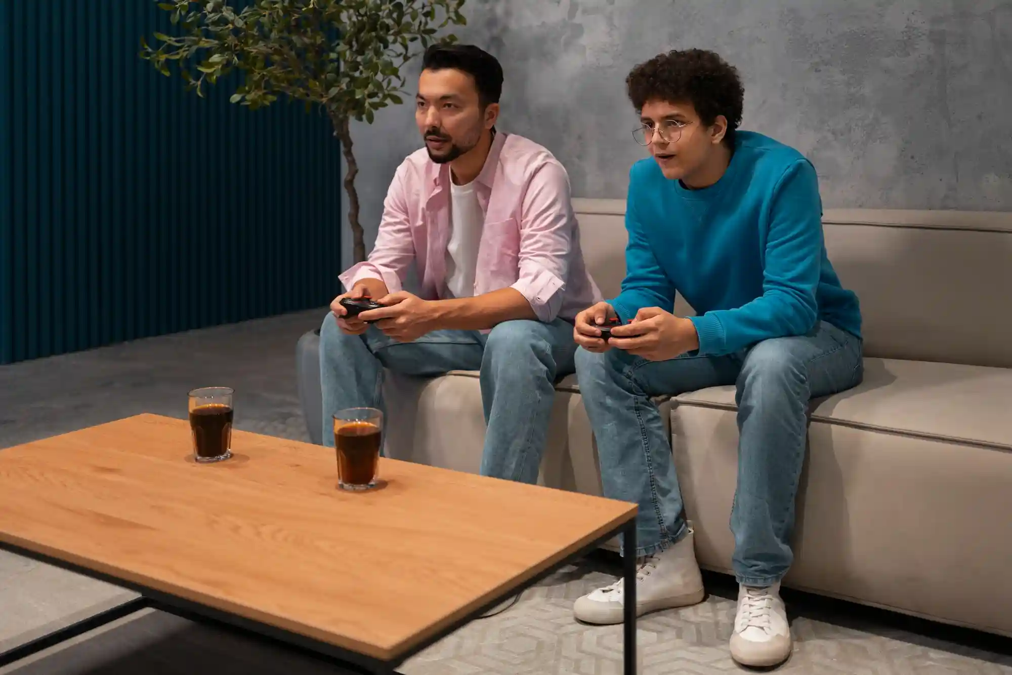 Two men sit on a sofa playing video games together with controllers, enjoying a social and immersive digital experience.