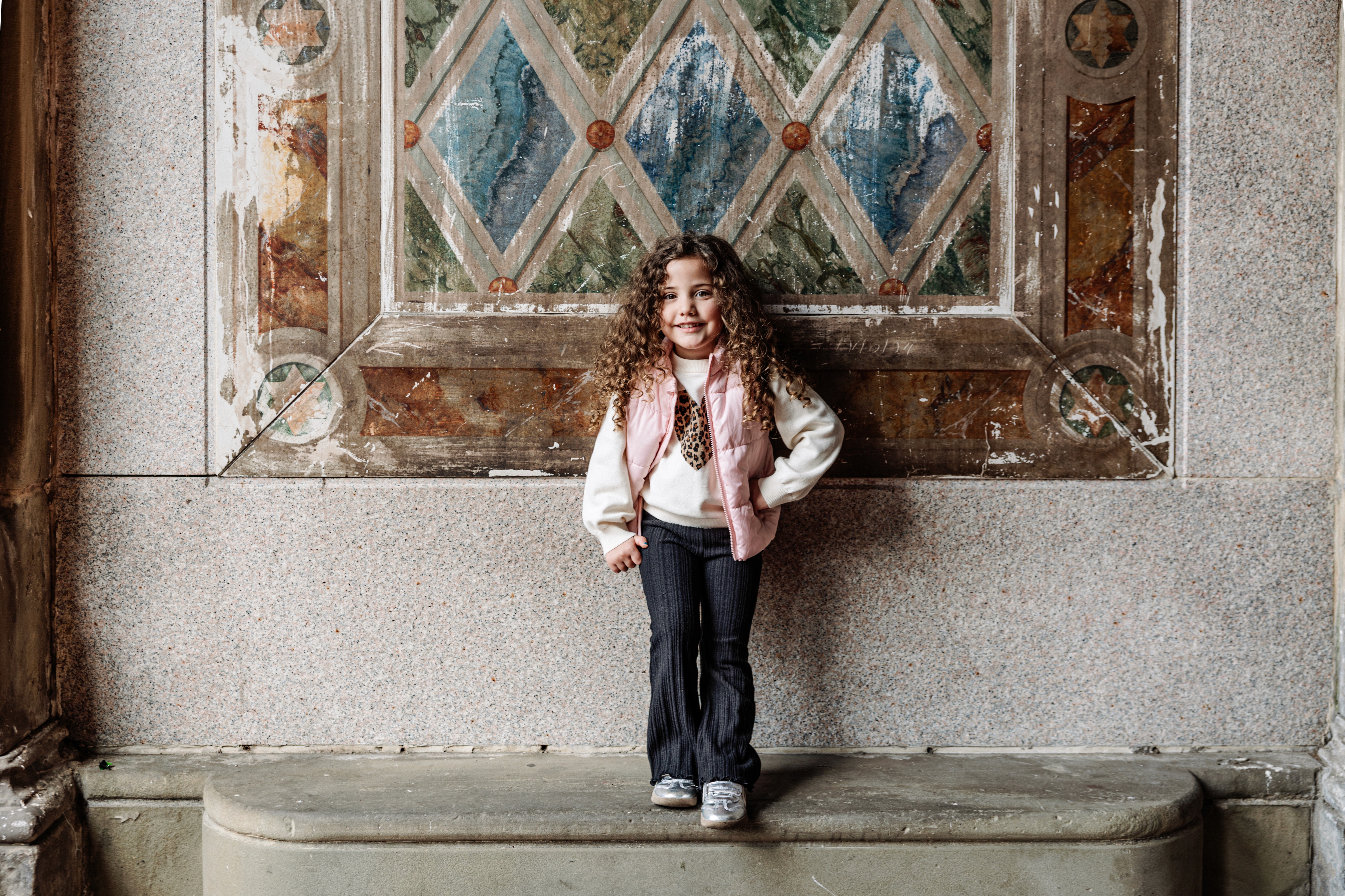 Adorable four year old with long curly hair posing at Bethesda Terrace in Central Park, NYC — natural, playful children's photography by Lizz Spano Photography, New York City family photographer.