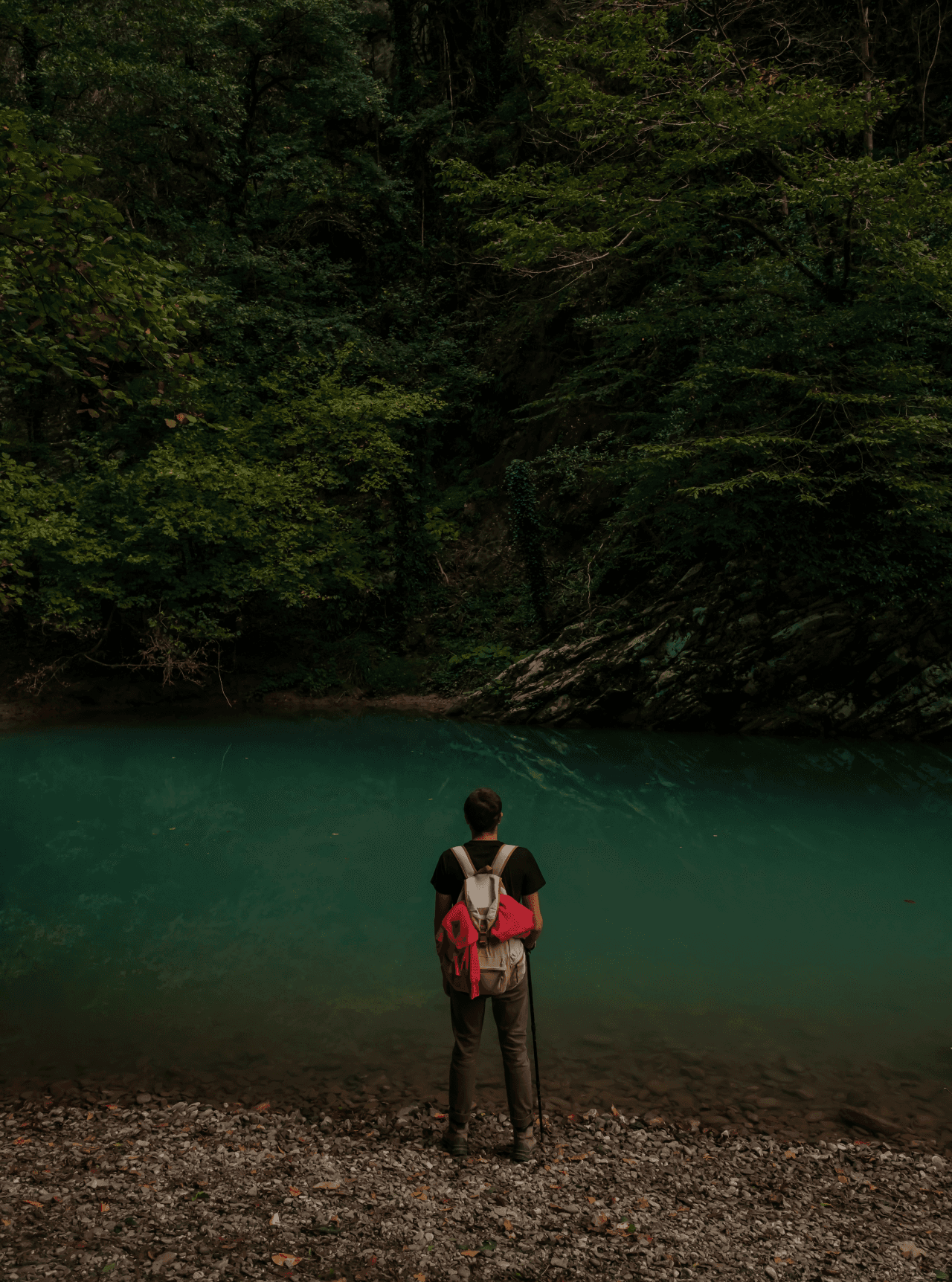 Hiker with a red backpack at the edge of an emerald forest pool