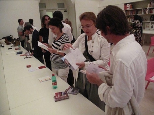 A photo of a group of persons standing near a table while checking some books and flyers.