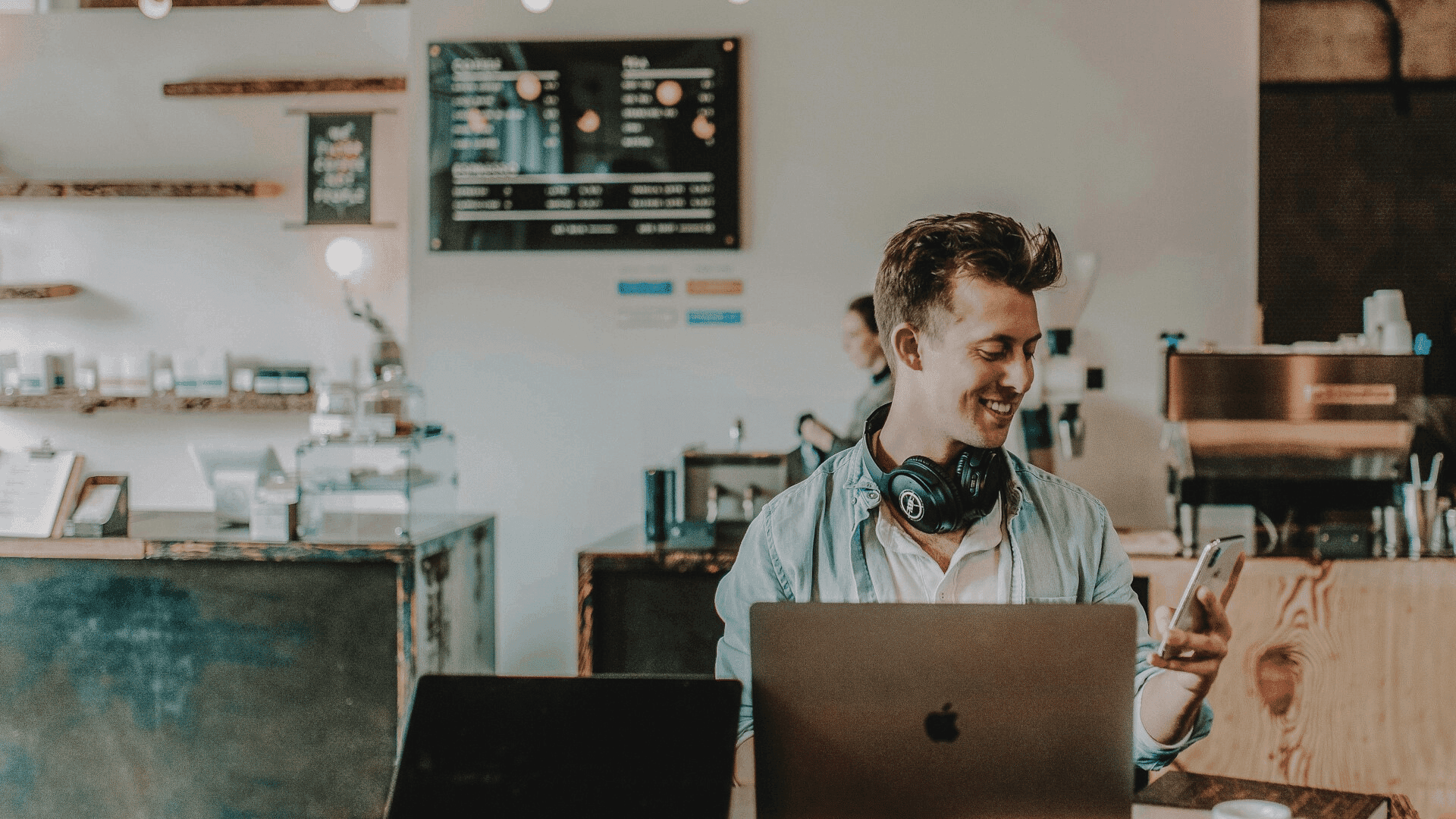 a man sitting down behind a laptop and smiling at his phone , probably depicting "how much does it cost to start an online business"