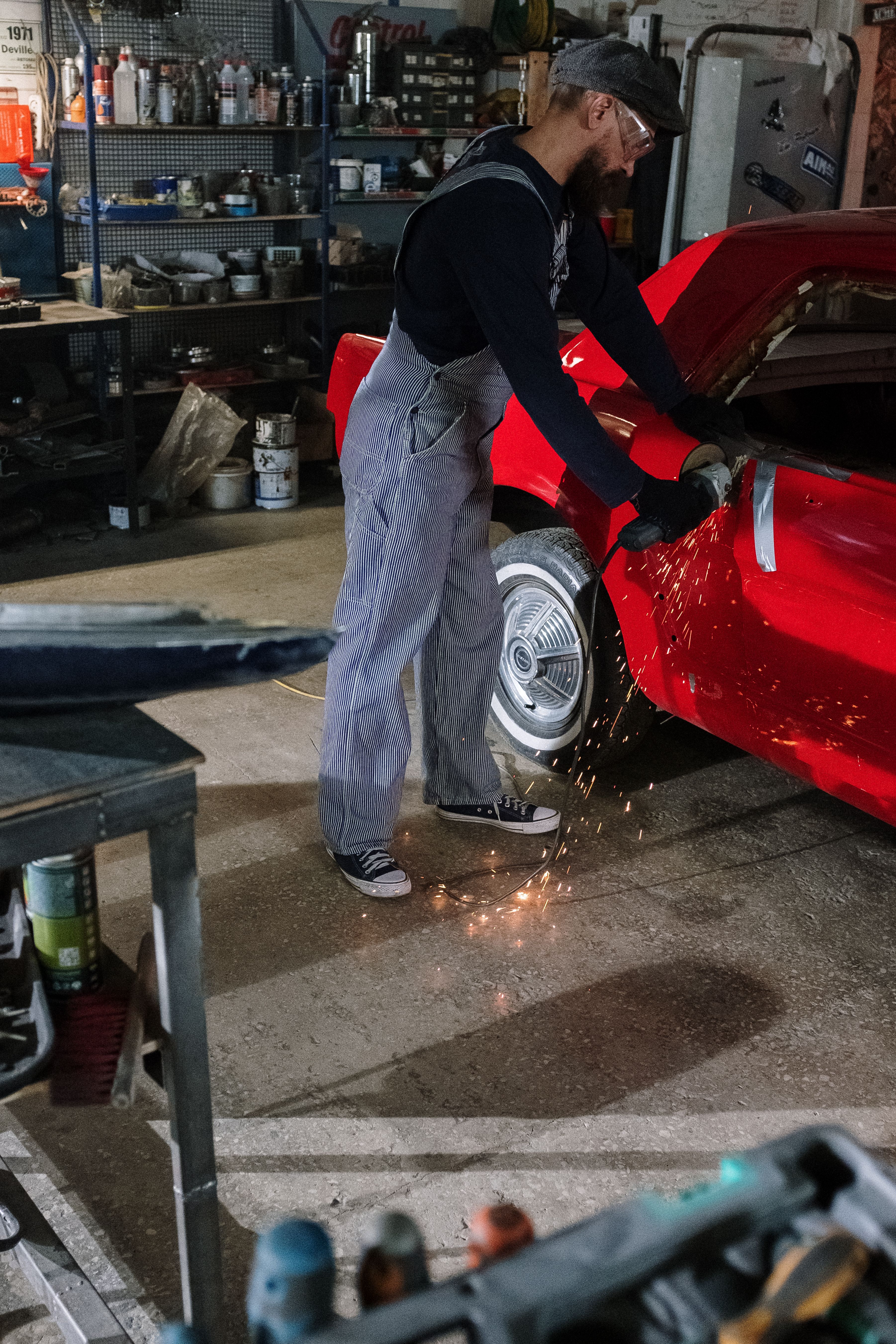Carrossier meulant un panneau de carrosserie d'une voiture rouge en atelier