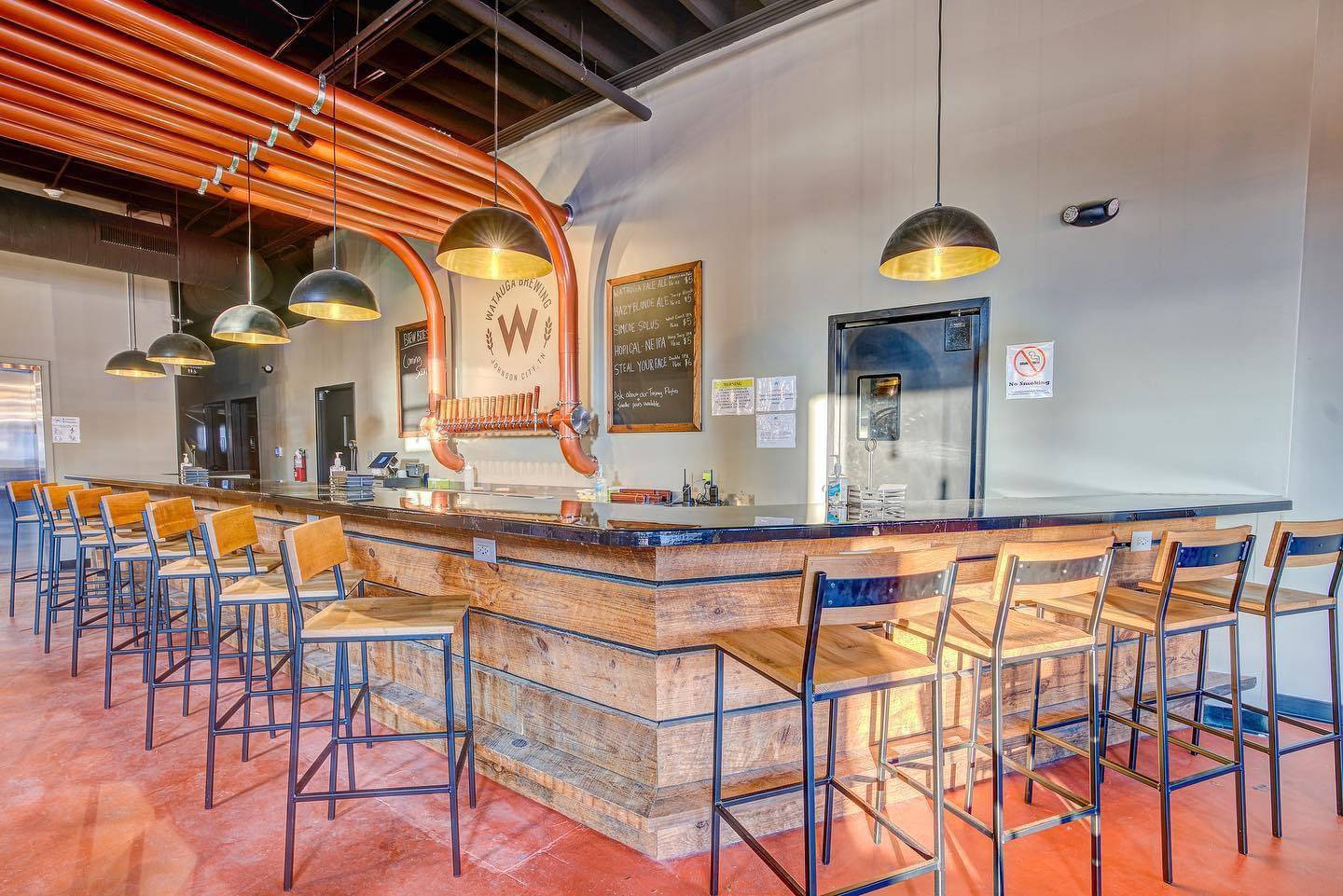 Modern restaurant interior featuring a bar with stools, bright lighting, and an open layout. Warm wooden accents.