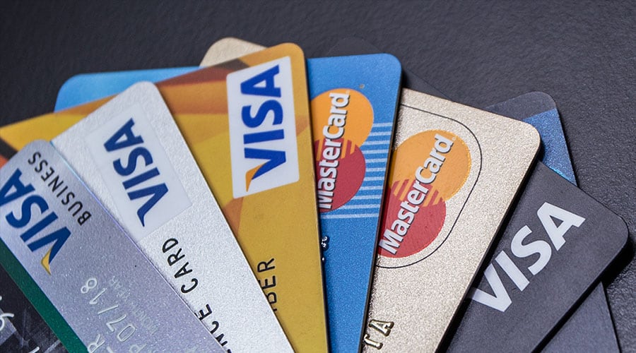 Aufgefächerte Visa- und Mastercard-Kreditkarten auf dunklem Untergrund, mit blauen, goldenen, silbernen und schwarzen Kartendesigns.
