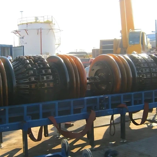 Große industrielle Walzen, die auf einen blauen Metallrahmen zum Transport geladen werden, mit einem Kran im Hintergrund.