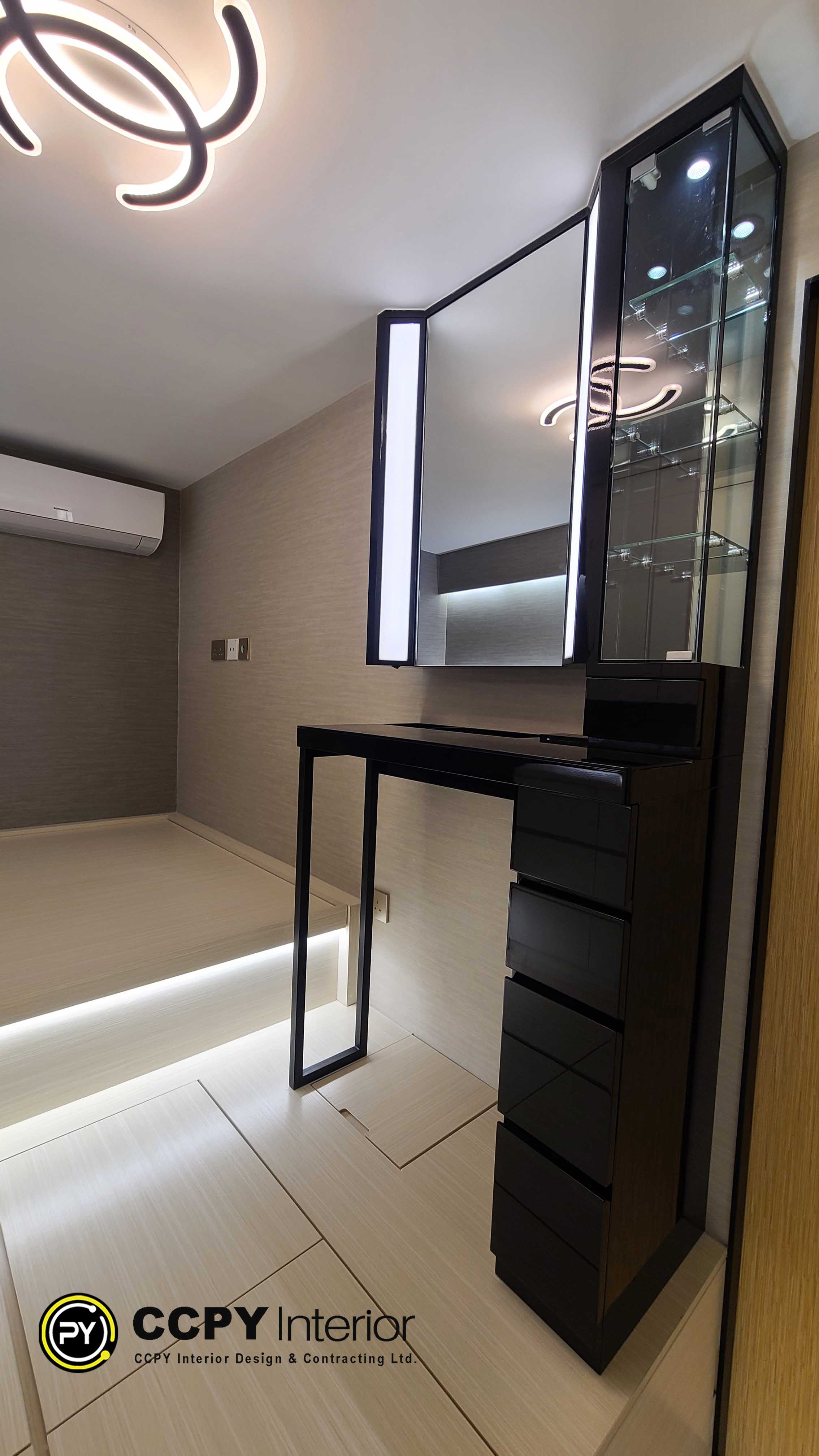 The selected region displays an interior view of a modern apartment renovation.Space FeaturesBuilt-in Furniture: Features sleek, dark cabinetry integrated with a light wood floor platform.Textured Walls: Covered in a neutral, grey textured wallpaper or paneling.Functional Layout: Includes a raised floor section, likely designed for hidden storage or a multi-functional seating area.Modern Fixtures: Shows a minimalist wall-mounted light fixture and clean glass shelving units.