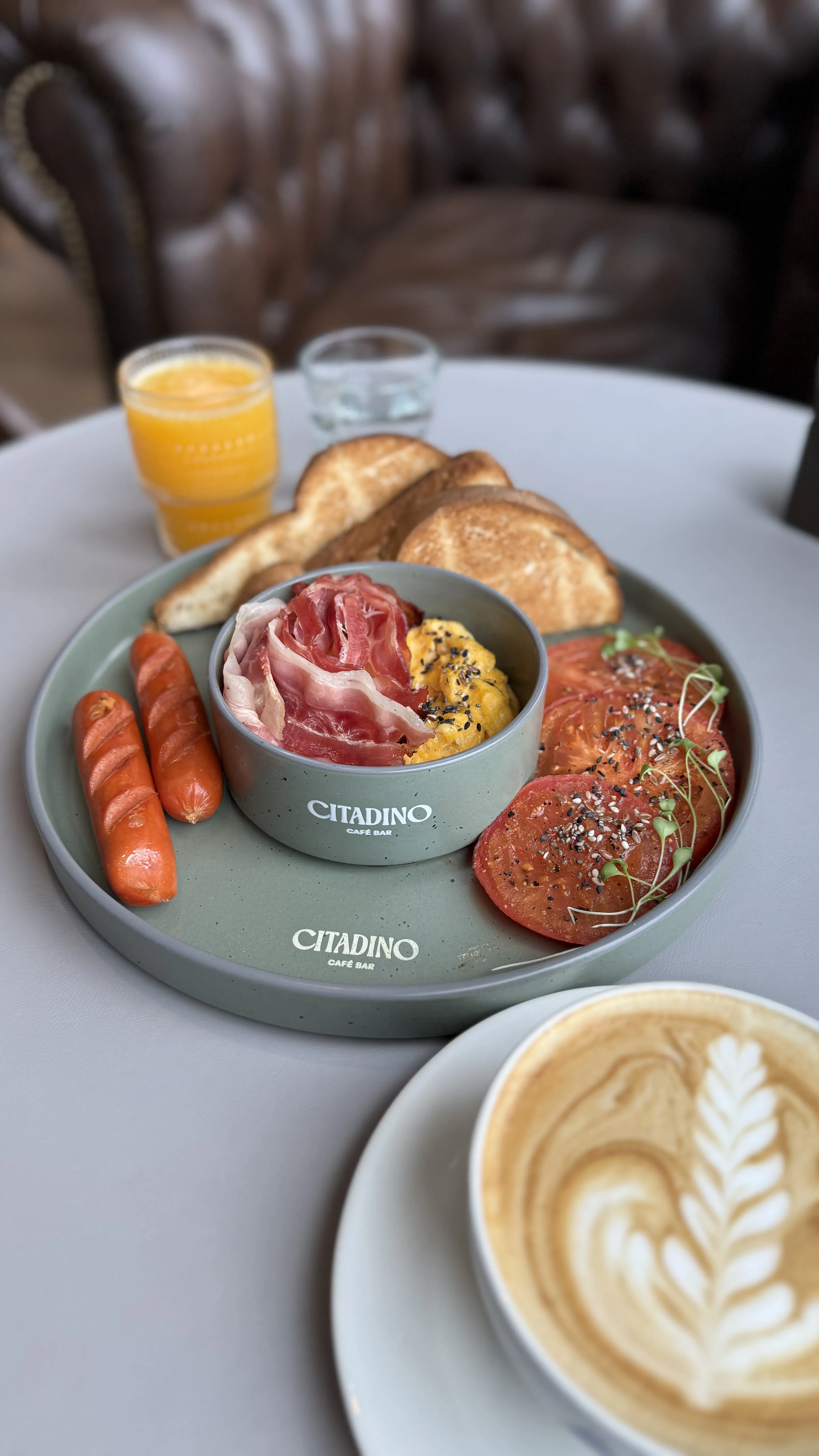 desayuno con salchichas, tostadas, jamón crudo, huevos revueltos con semillas, jugo de naranja, agua y café.  