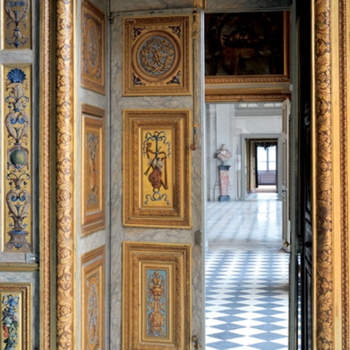 華麗的門口，裝飾著精緻的金色和色彩斑斕的設計，通往一個擁有棋盤地磚和古典雕像的大廳。