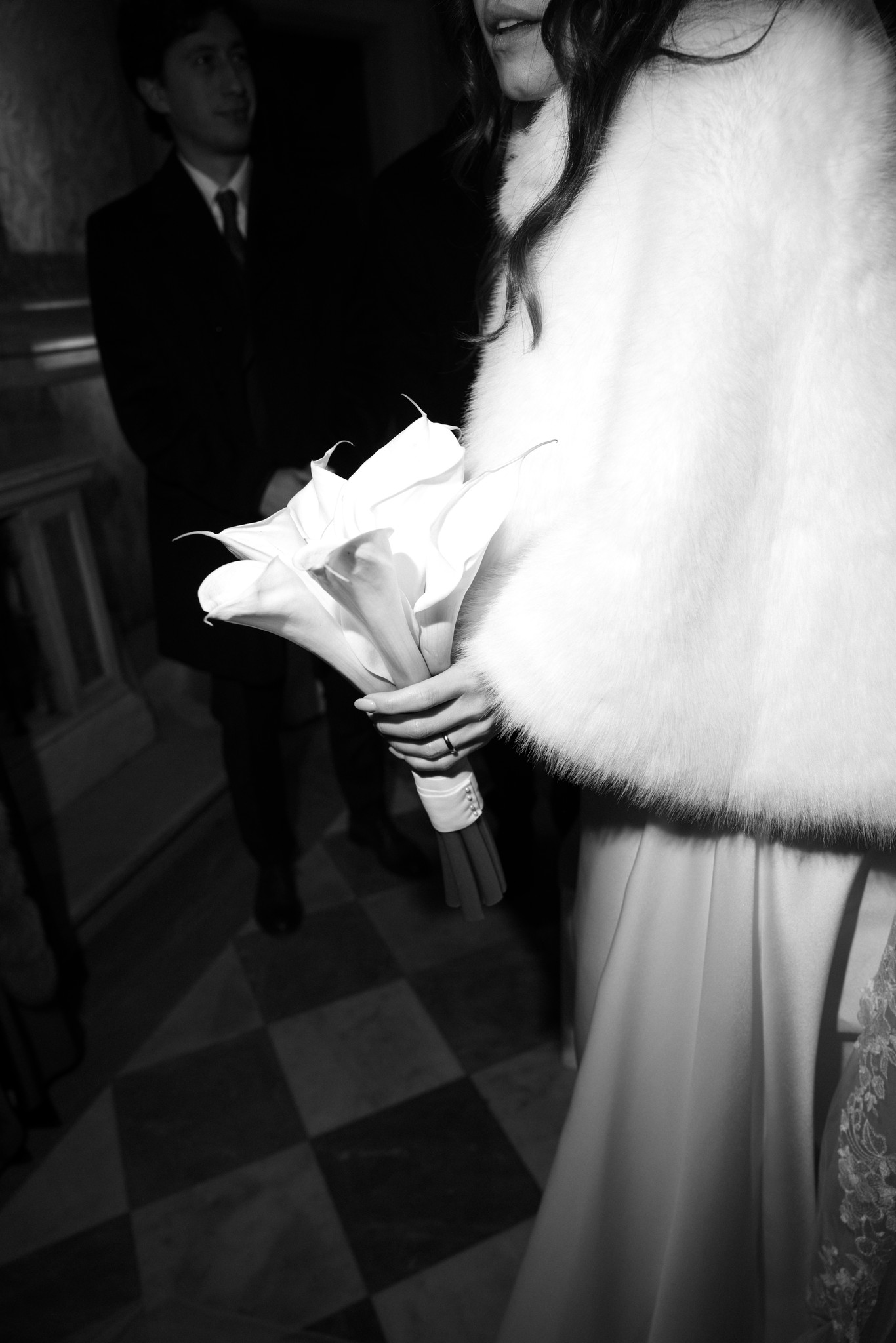 Sposa in abito mikado con bouquet di calle, sposo sfumato sullo sfondo, reportage matrimoniale al Circolo di Lettura a Parma