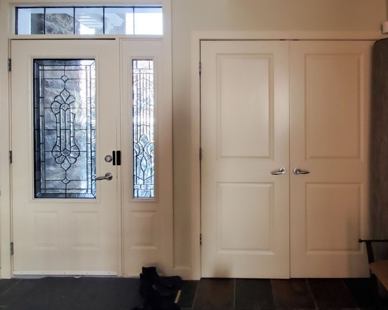 An entryway with a white front door with glass insert and a double doored coat closet to the right.