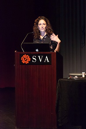 Portrait of a woman giving a speech from a wooden stand with the SVA logo on it
